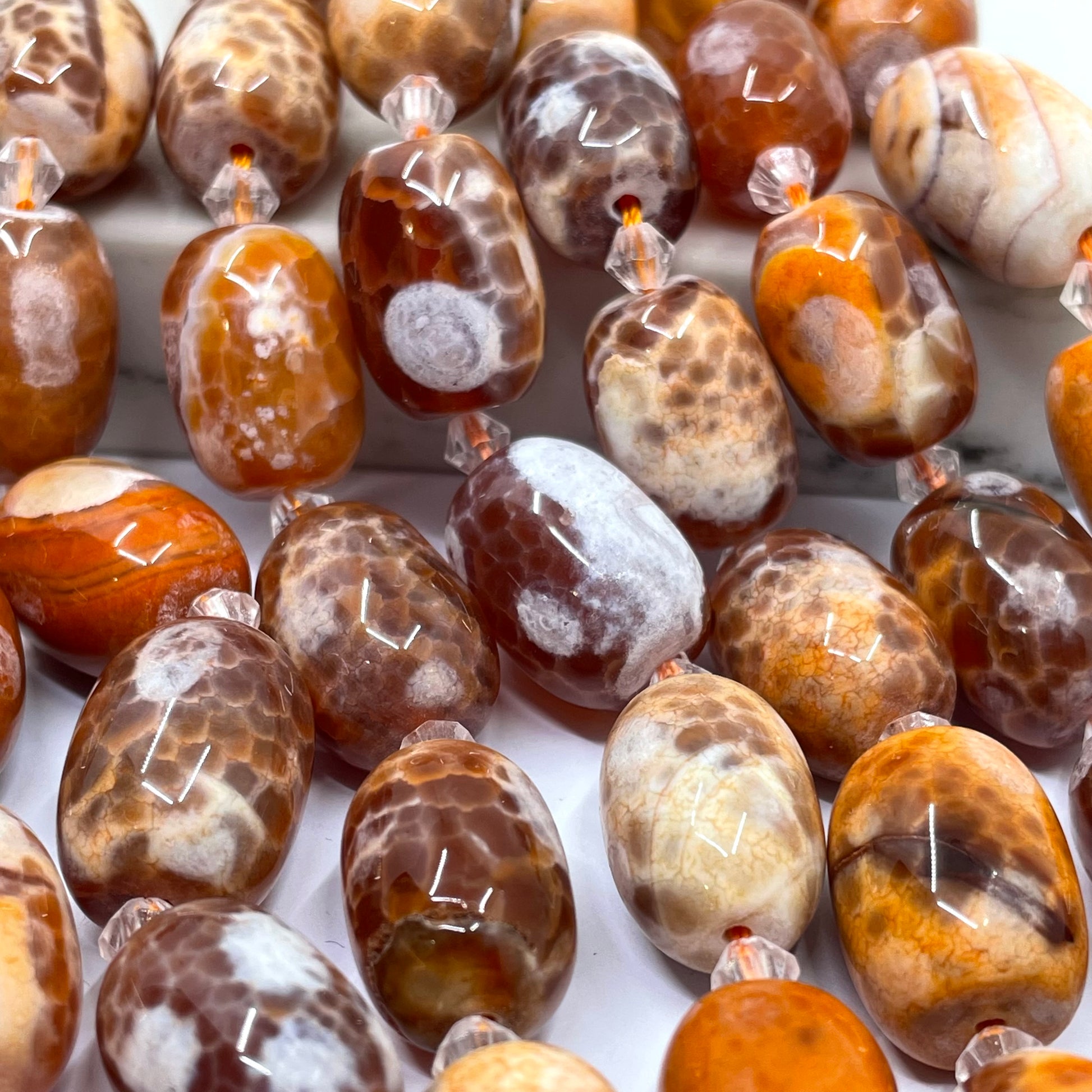 A close-up of polished brown and cream agate stone beads with natural marbled patterns, strung on clear cords.