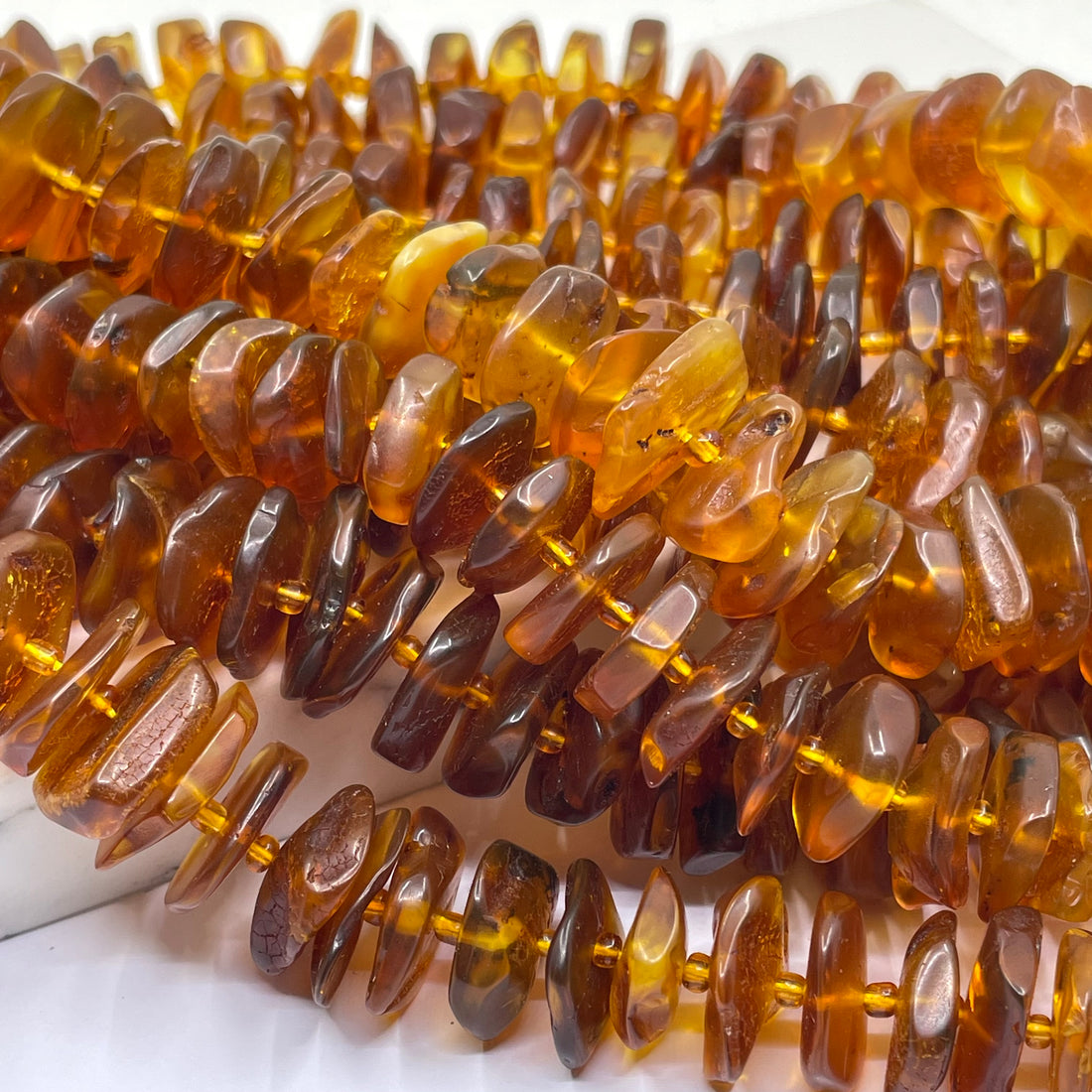 A close-up of multiple strands of polished amber chip beads in warm translucent brown and amber tones, strung on gold-tone wire.