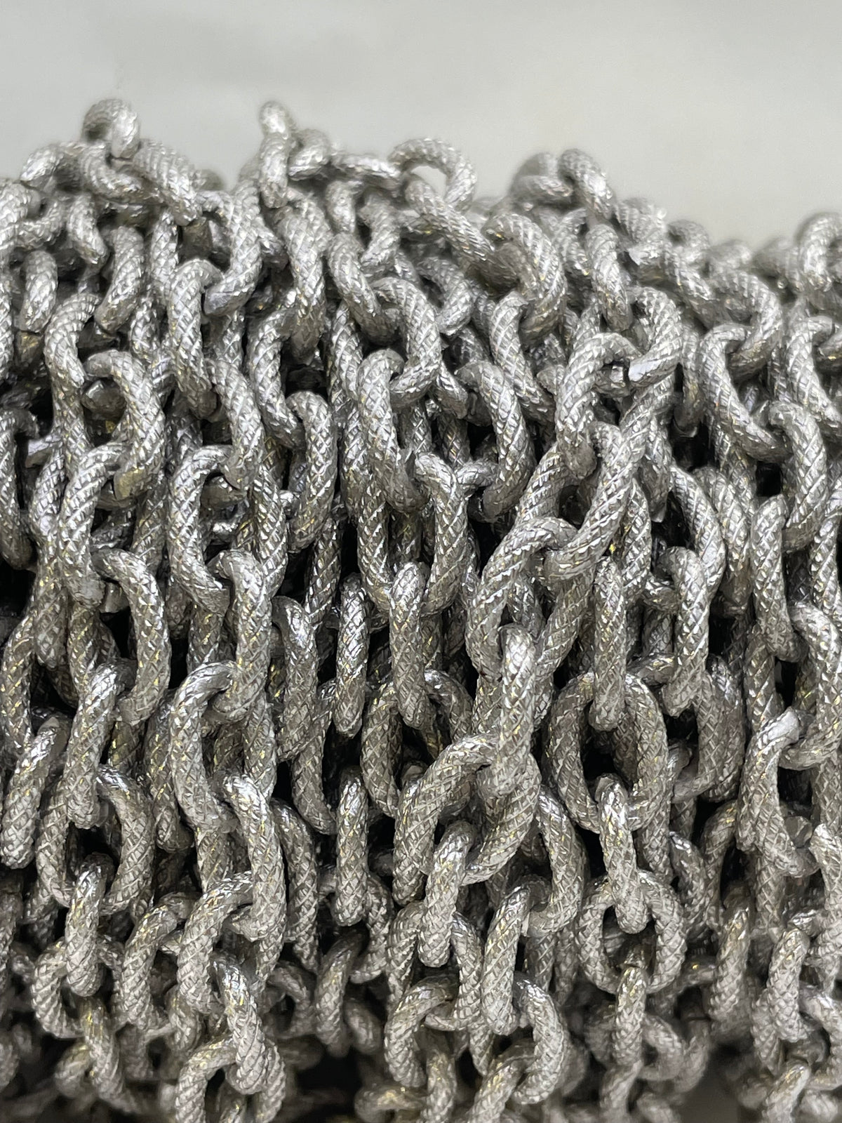 A close-up of a coiled spool of silver metallic chain links against a light gray background.