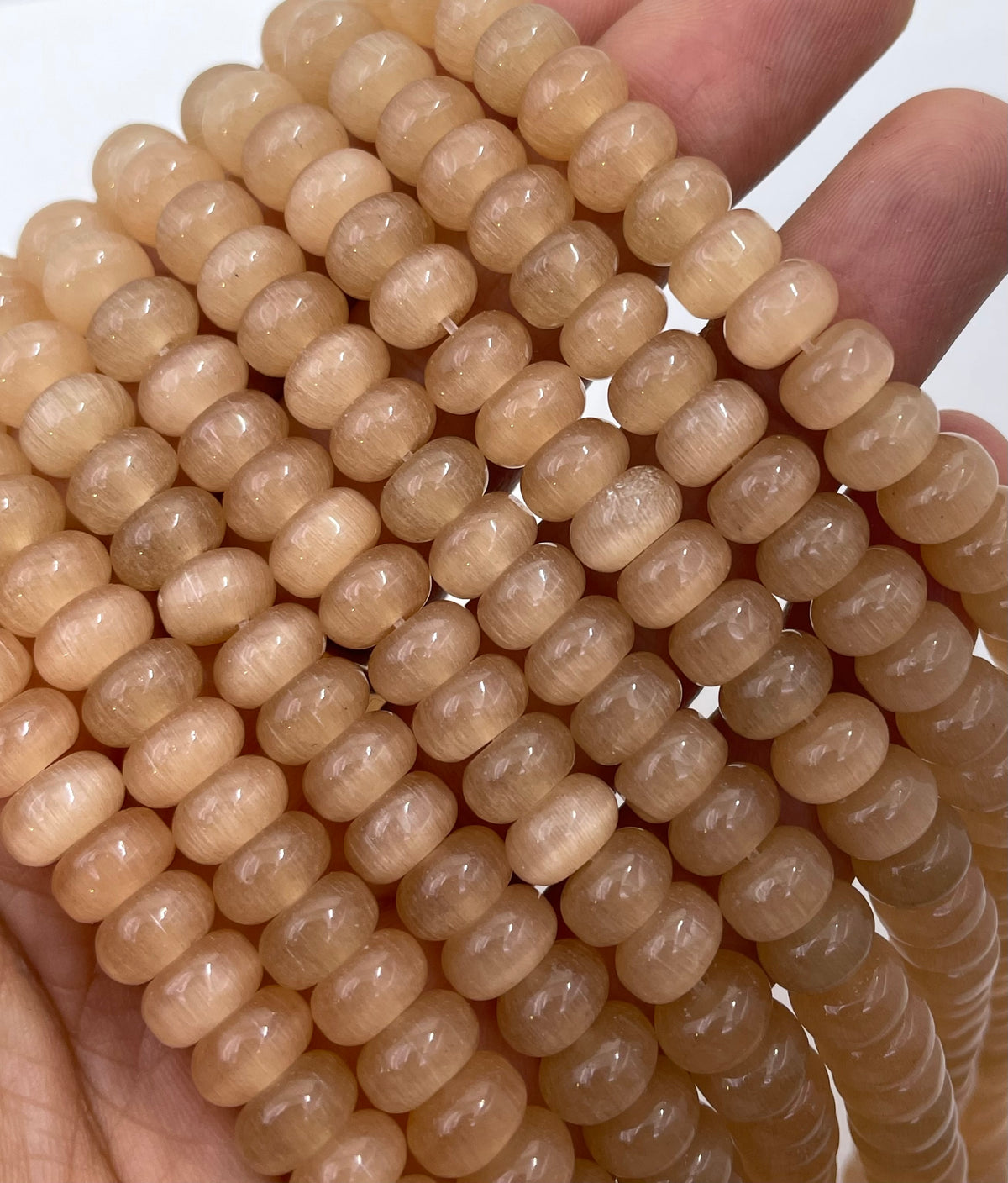 Multiple strands of smooth, cylindrical cats eye beads held in a hand against a plain white background.