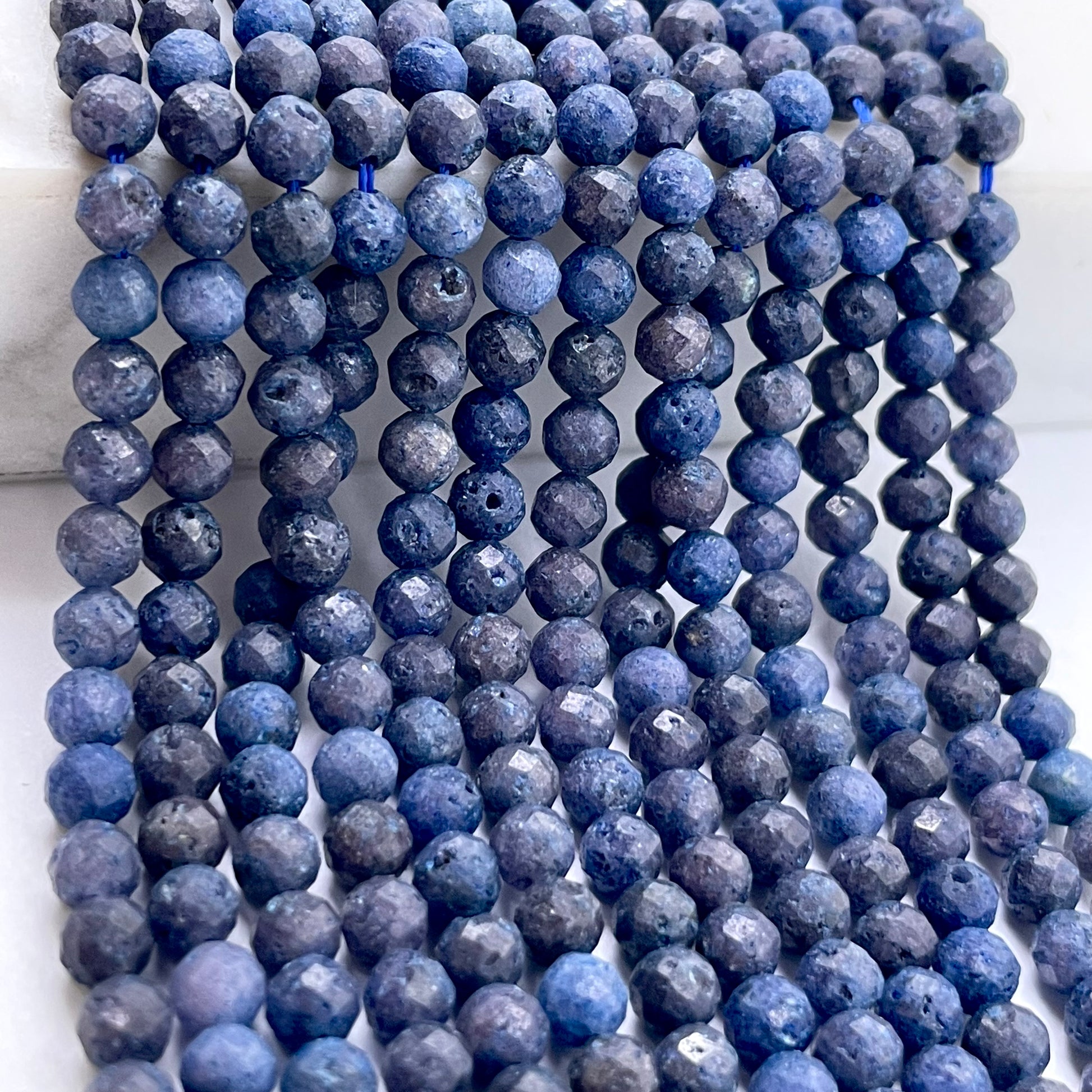 Multiple strands of faceted round sapphire beads, arranged vertically on a light background.