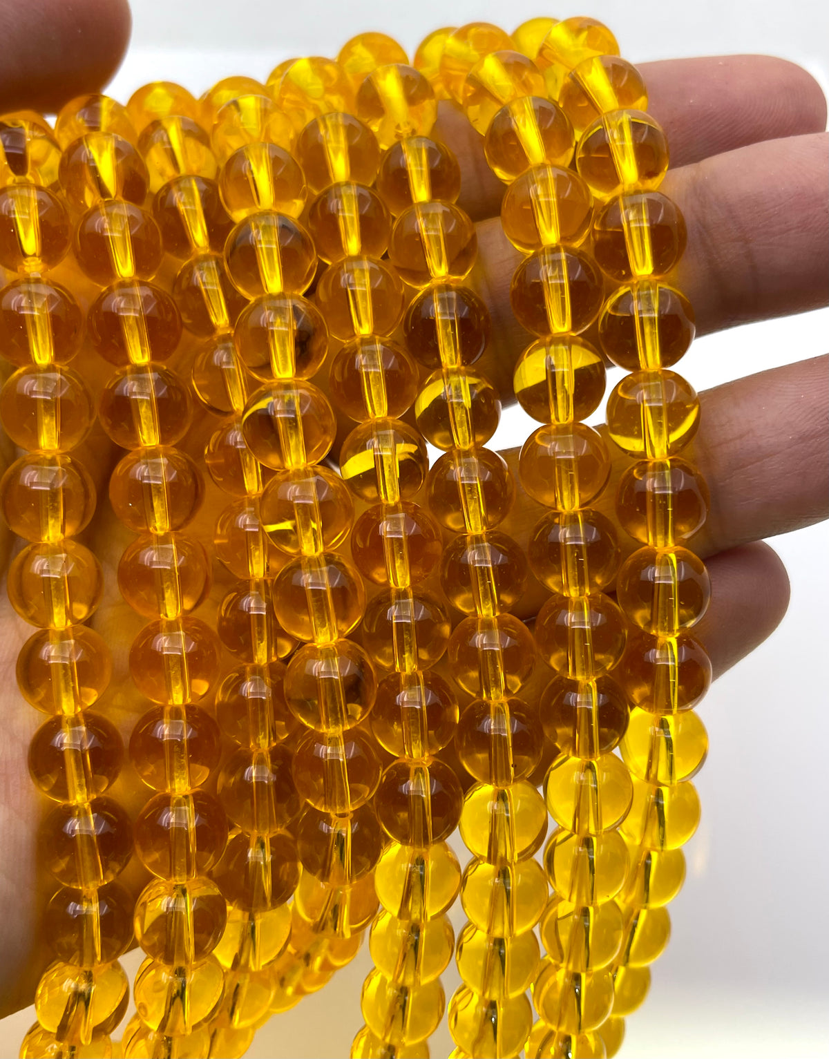 Multiple strands of translucent amber-yellow round beads held in a person's hand against a plain light background.