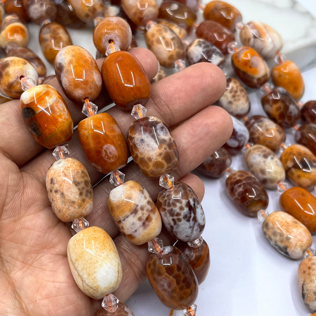 A close-up of polished agate stone beads with natural mottled patterns in shades of brown, orange, cream, and white, strung on clear cords.
