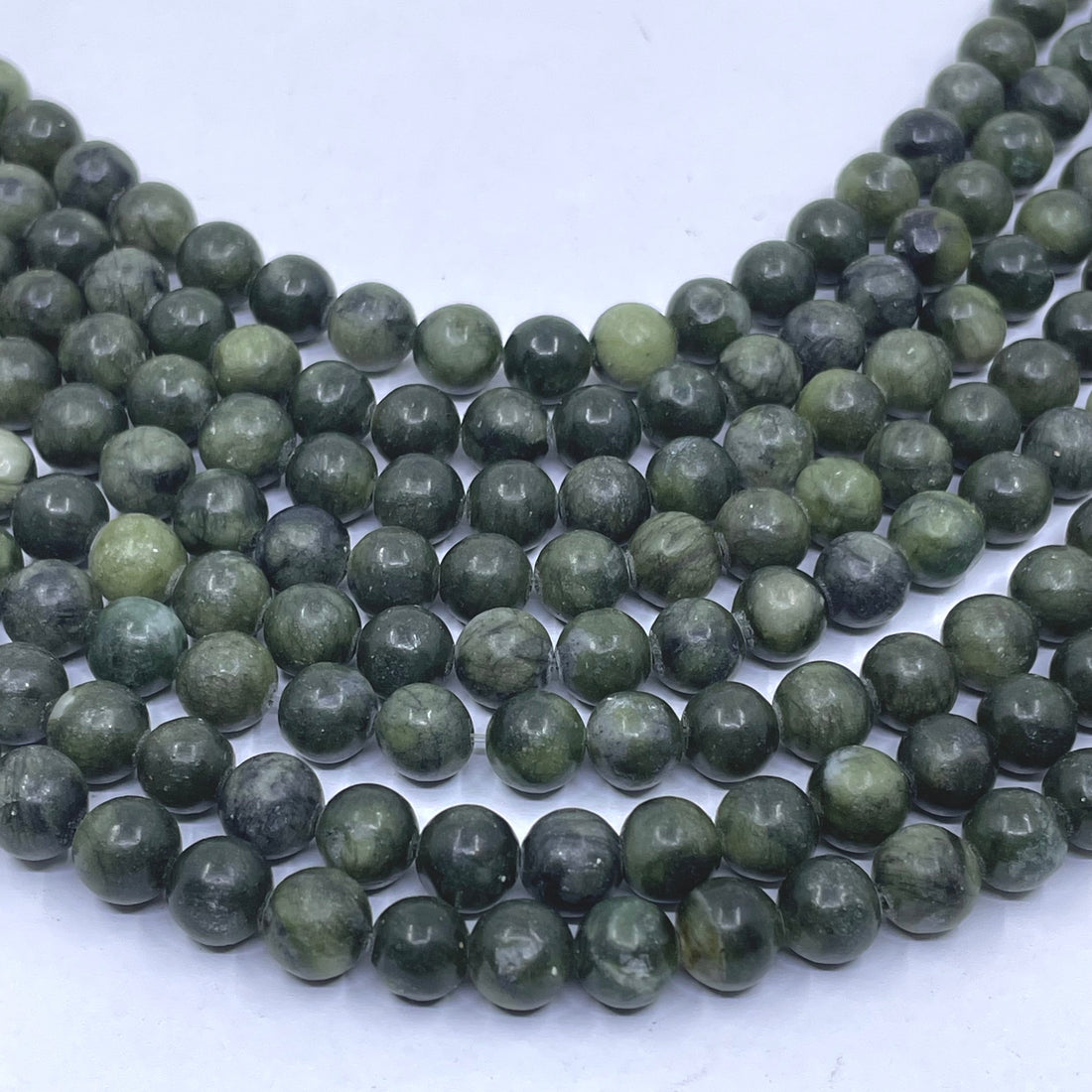 Multiple strands of round green jade stone beads arranged in curved rows on a plain white background.