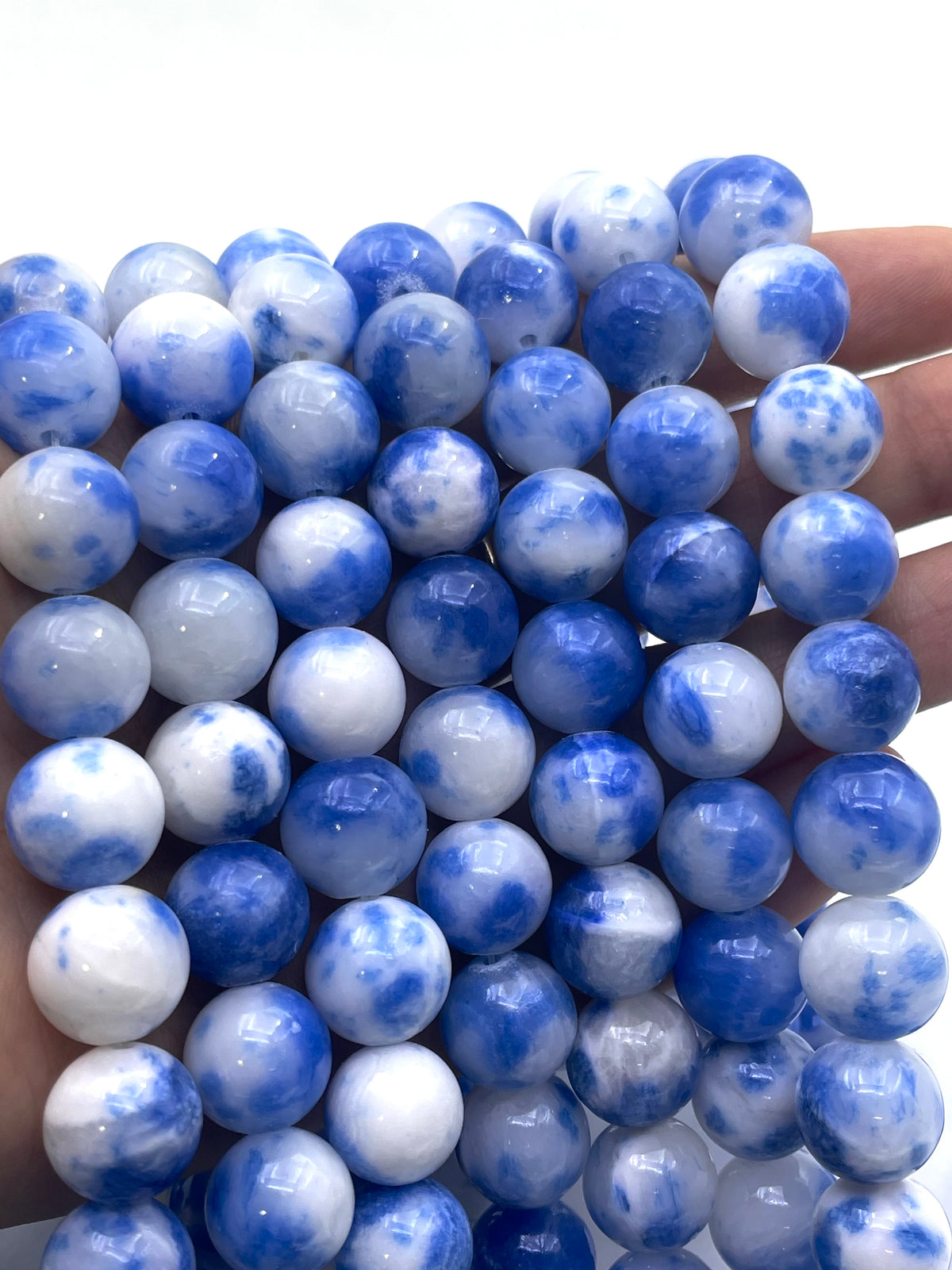 A close-up of a hand holding a strand of polished round blue persian jade beads in blue and white marbled stone.