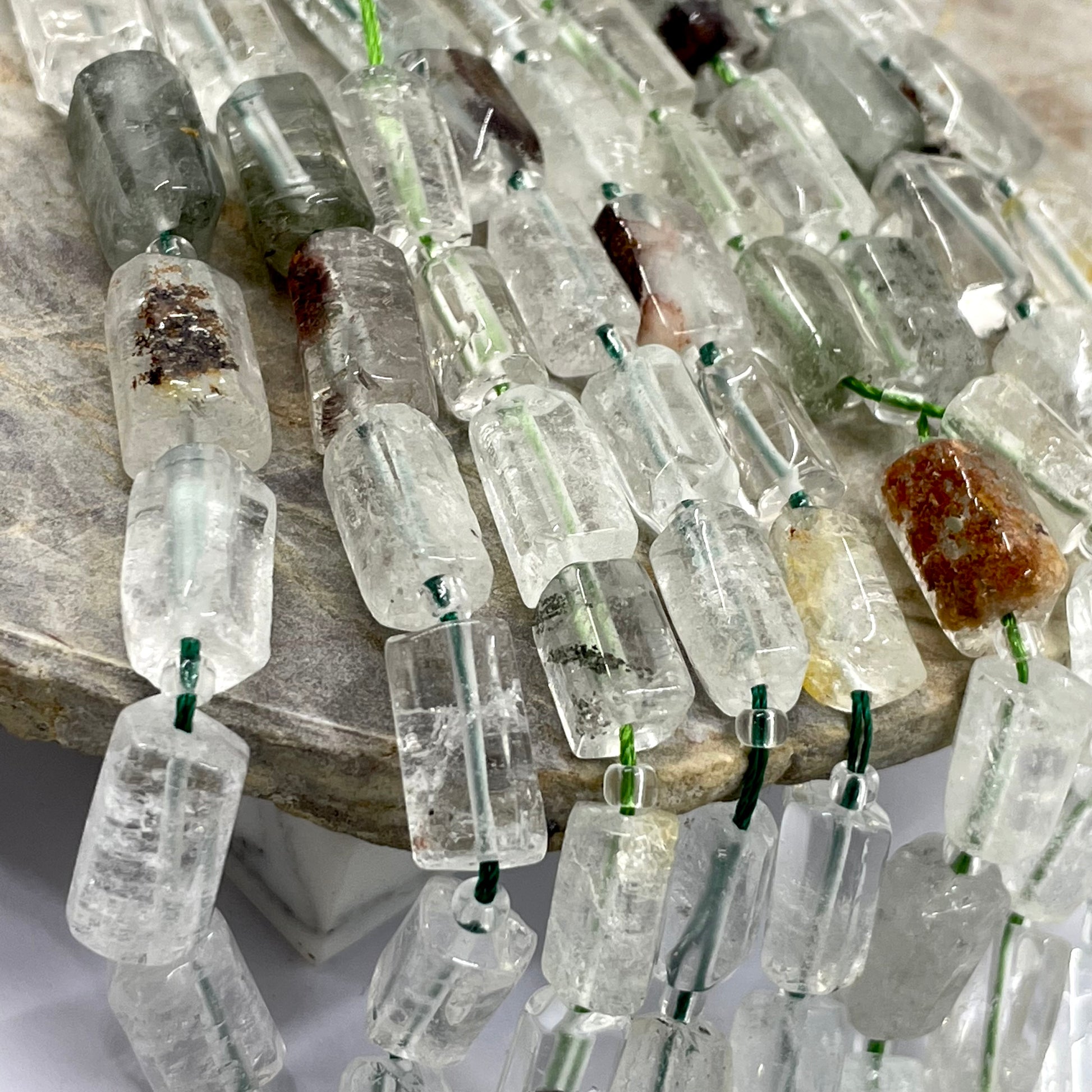 Garden quartz crystal beads with natural inclusions and green string, displayed on a stone surface.