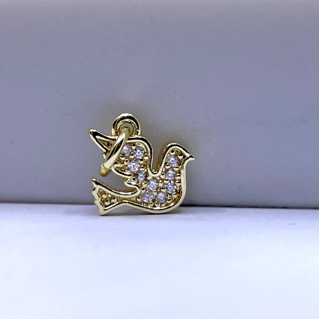 A gold bird-shaped charm or pendant decorated with small clear stones, photographed on a plain light gray background.