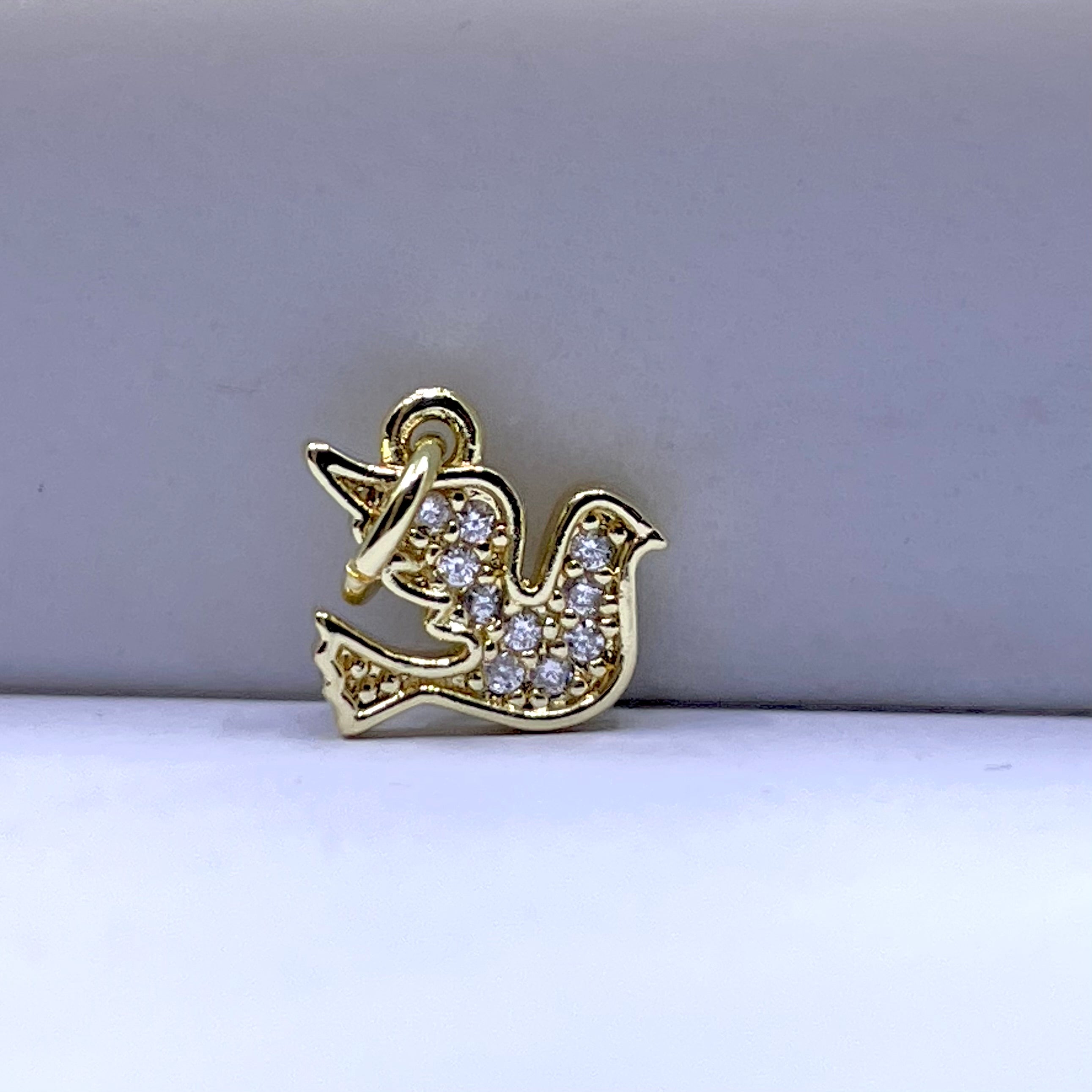A gold bird-shaped charm or pendant decorated with small clear stones, photographed on a plain light gray background.