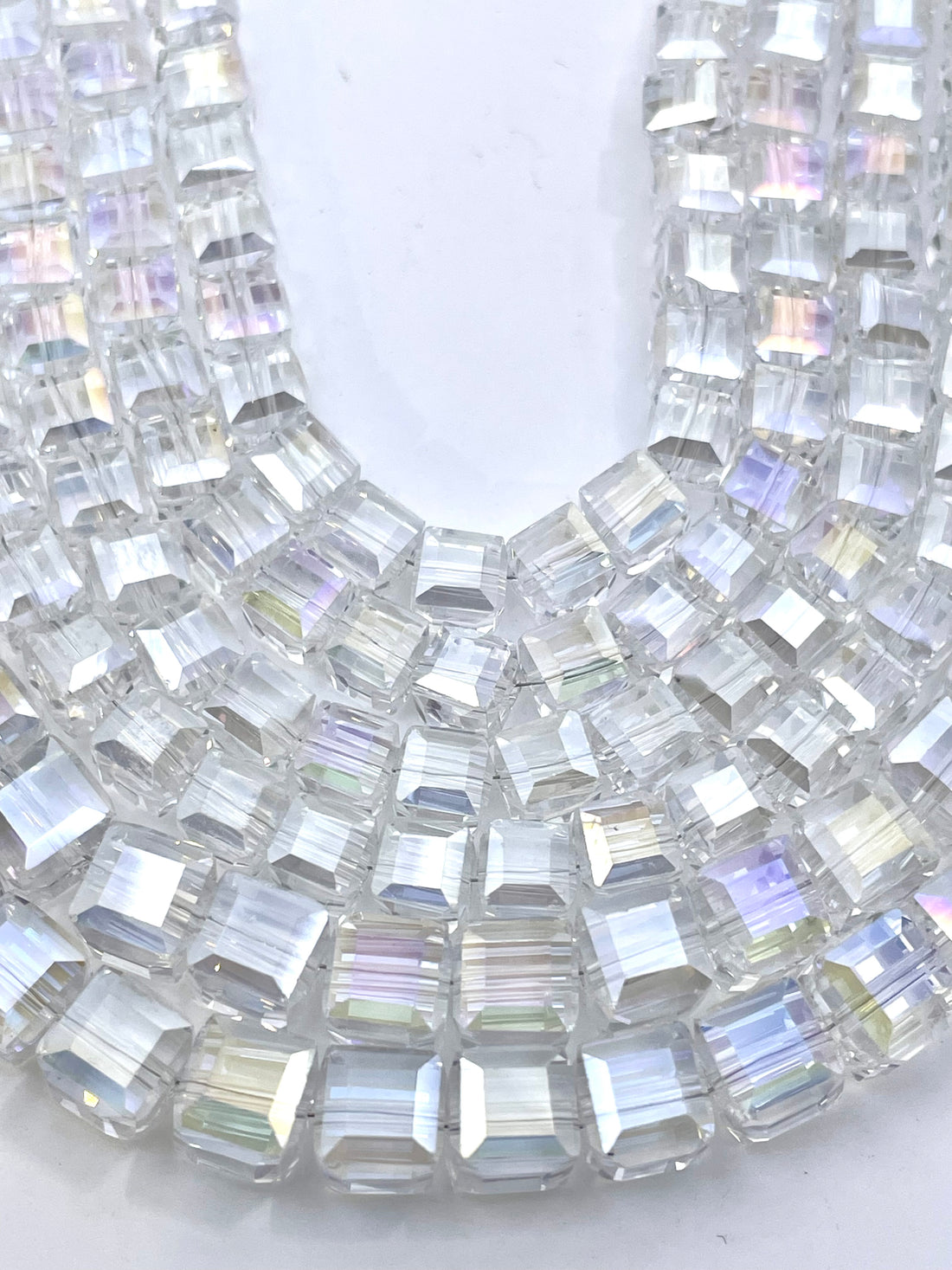 Clear cube faceted beads with an iridescent AB finish, draped over a hand to show their transparent and rainbow-reflective quality.
