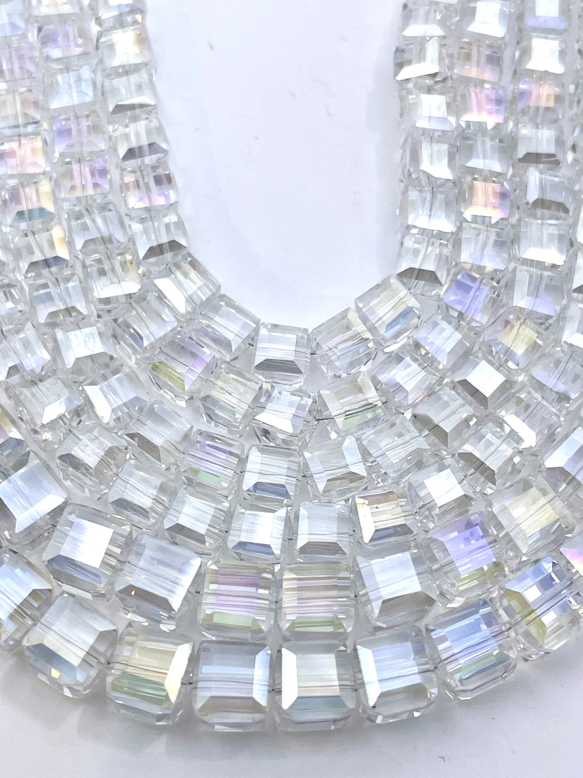 A close-up of a curved arrangement of clear cube glass faceted beads with an iridescent, rainbow-reflective coating on a white background.