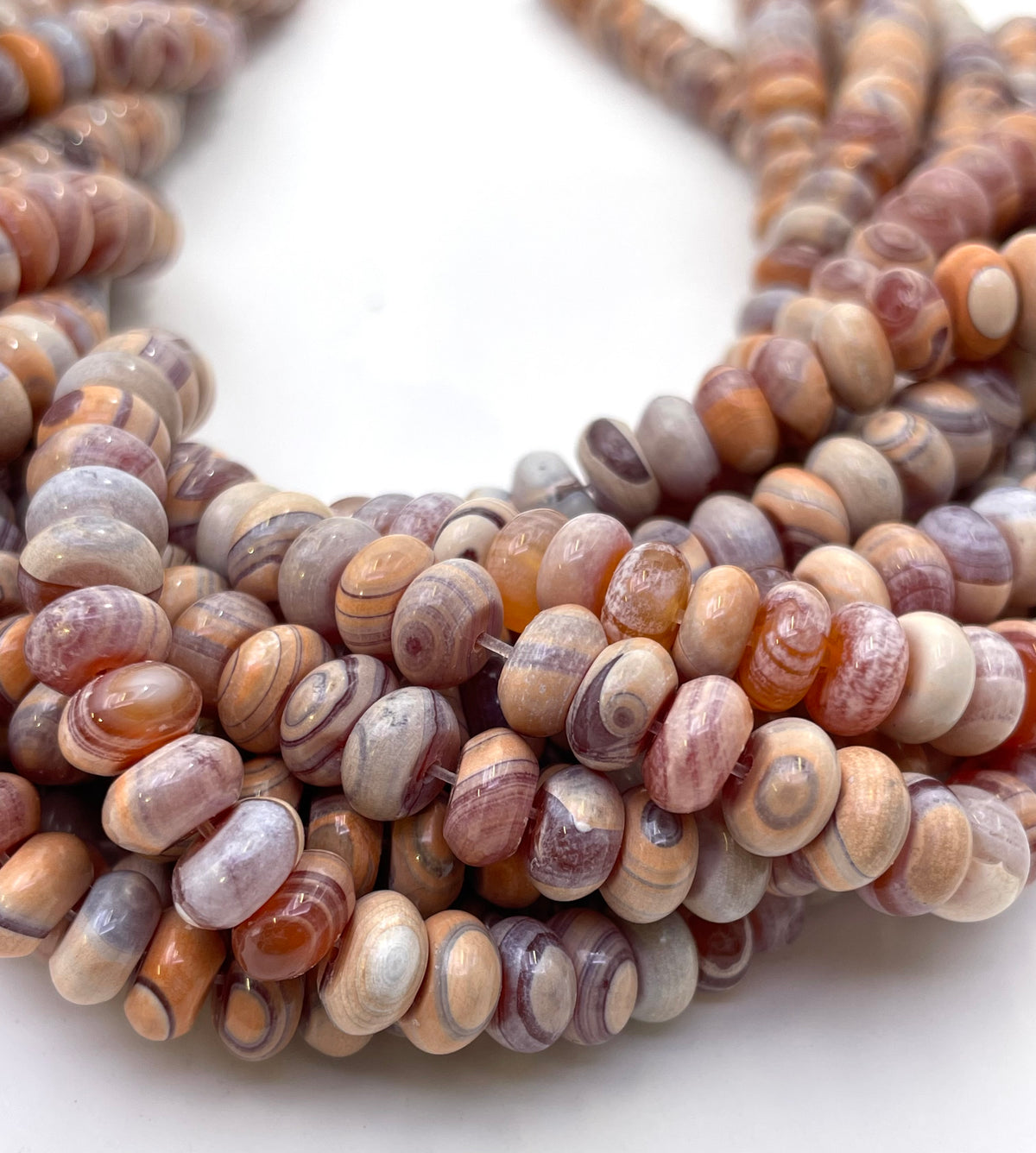 Close-up of a strand of smooth donut gobi agate beads with a marbled, swirled pattern in earthy tones of brown, beige, gray, and white, arranged in a loop on a plain white background.