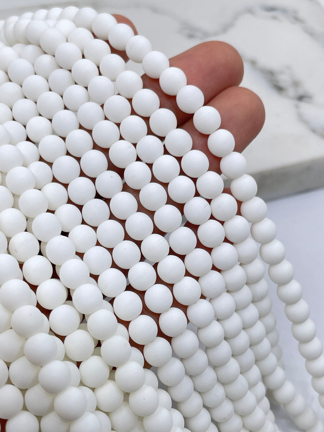 Velvet White round glass beads arranged in parallel strands on a light marble surface.