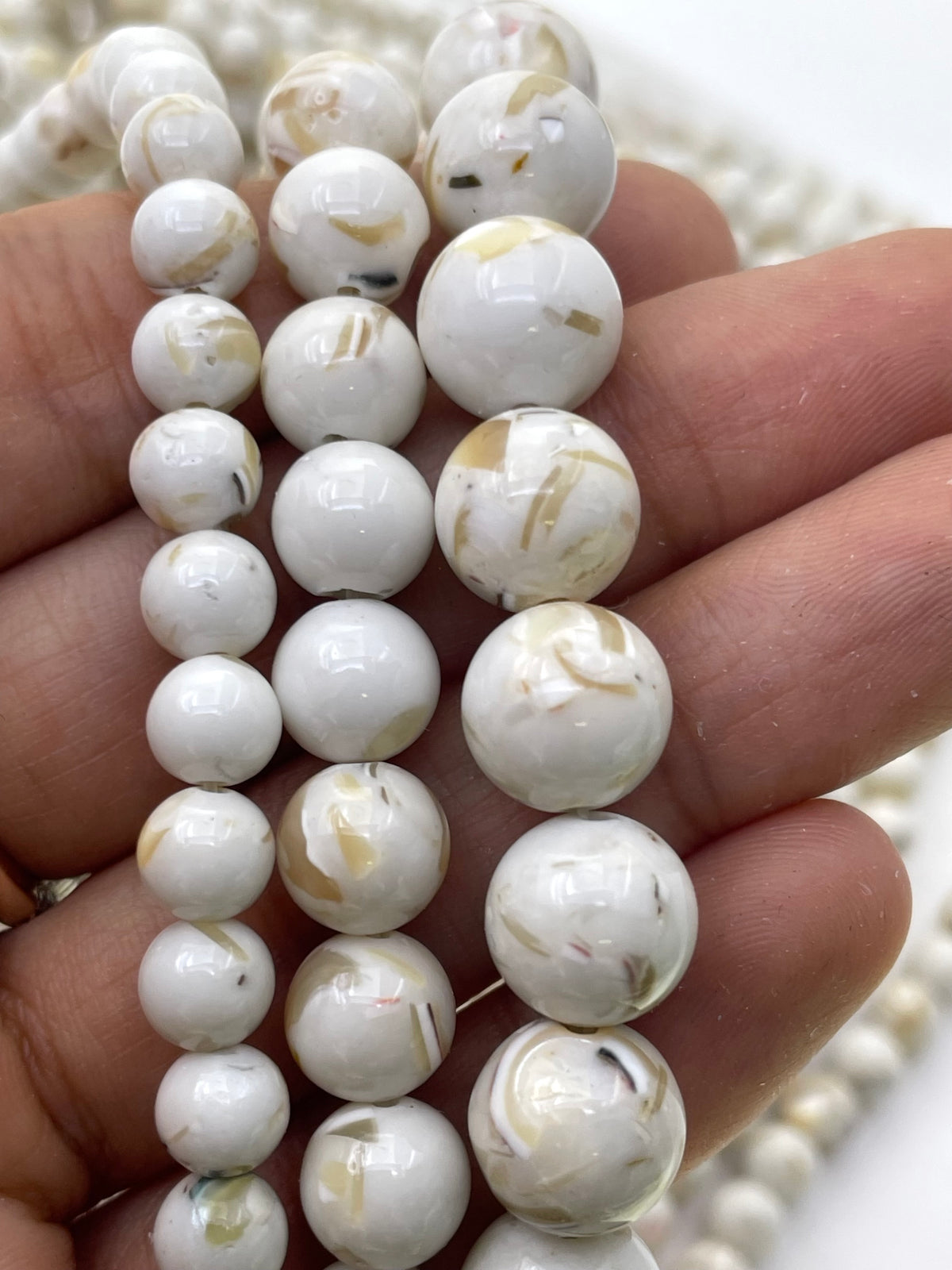Ivory marbled mop beads with natural inclusions, shown threaded on strands and held in a hand.
