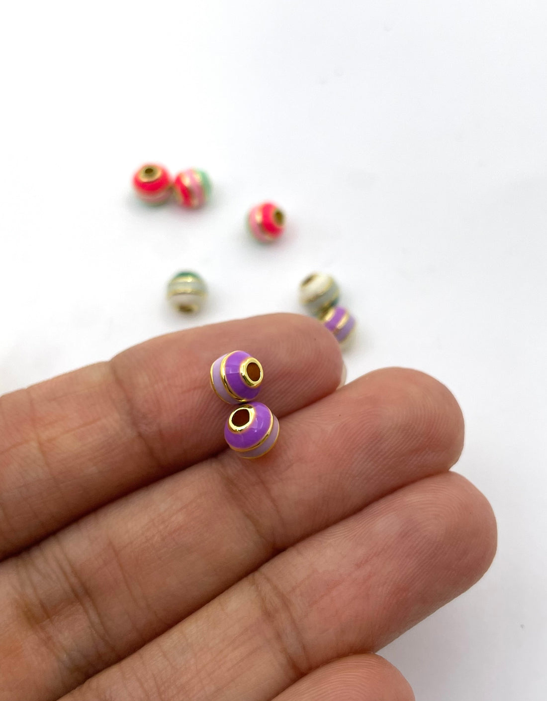 A group of colorful striped brass bead charms with gold-plated edges, displayed on a clean white background.