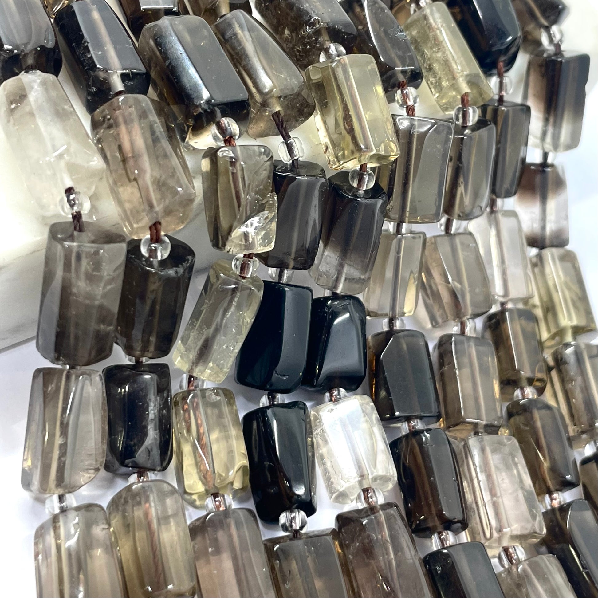 A close-up of a beaded strand featuring rectangular smoky crystal beads in various shades of gray, black, and translucent white.