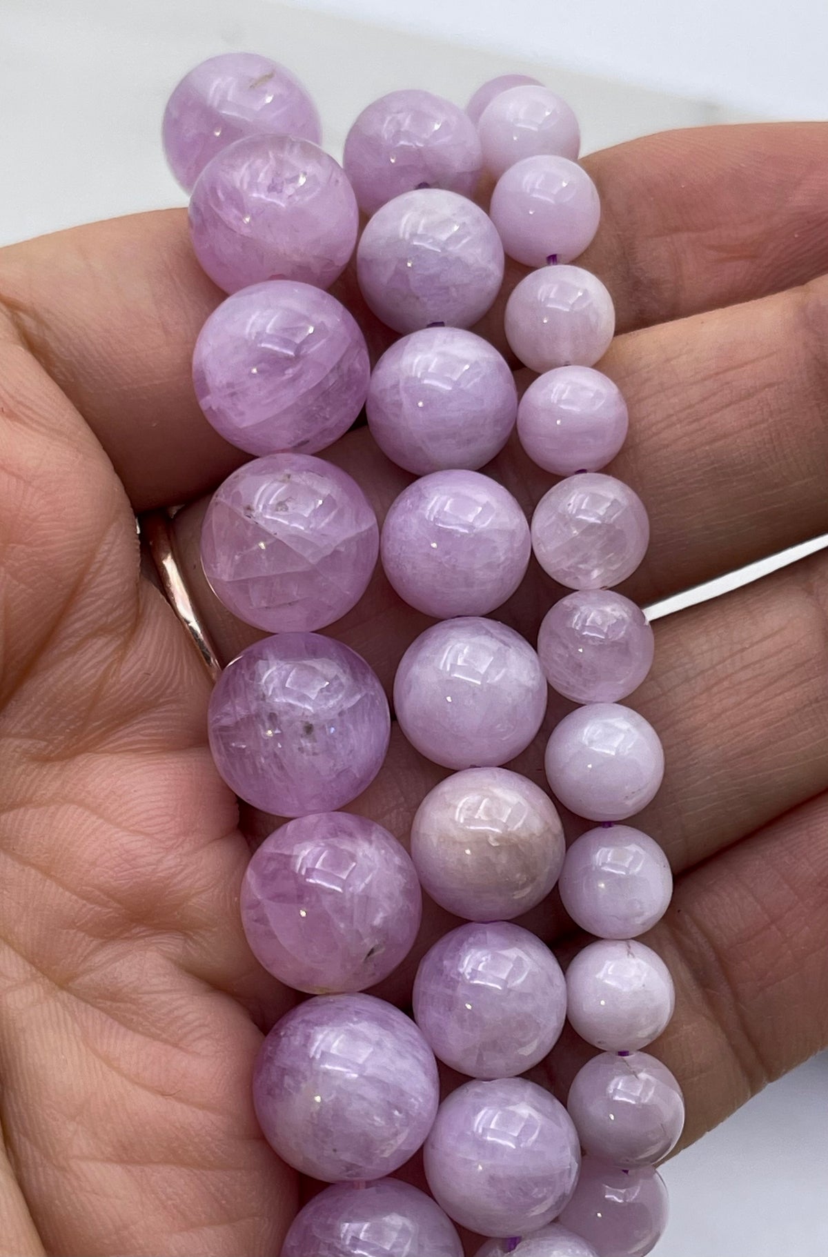 A close-up of a hand holding multiple strands of faceted light purple kunzite  beads, likely from a crystal or gemstone bead strand bundle.
