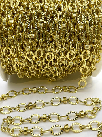 A close-up of a gold-colored chain link accessory, showing a spool of the chain in the background and several individual links draped in the foreground on a white surface.