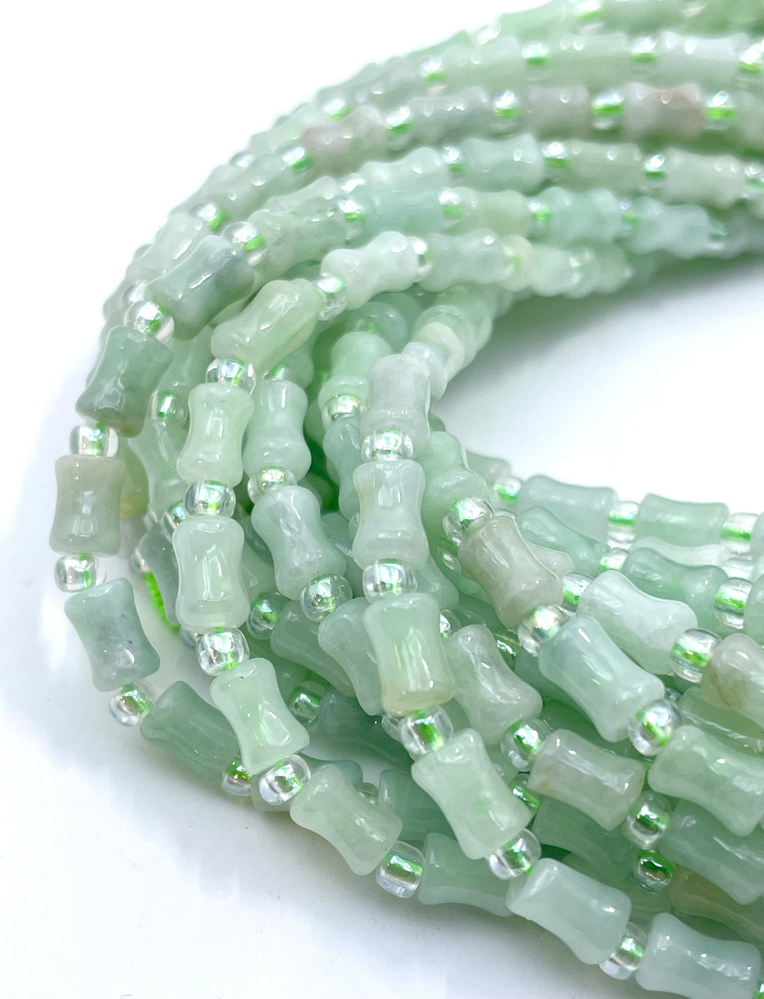 Green Burma Jade cylindrical beads with small silver spacer beads, held in a hand to show the strand length and texture.