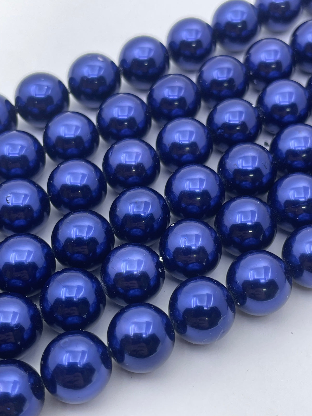 A close-up of glossy dark blue beads arranged in rows on a plain white background.