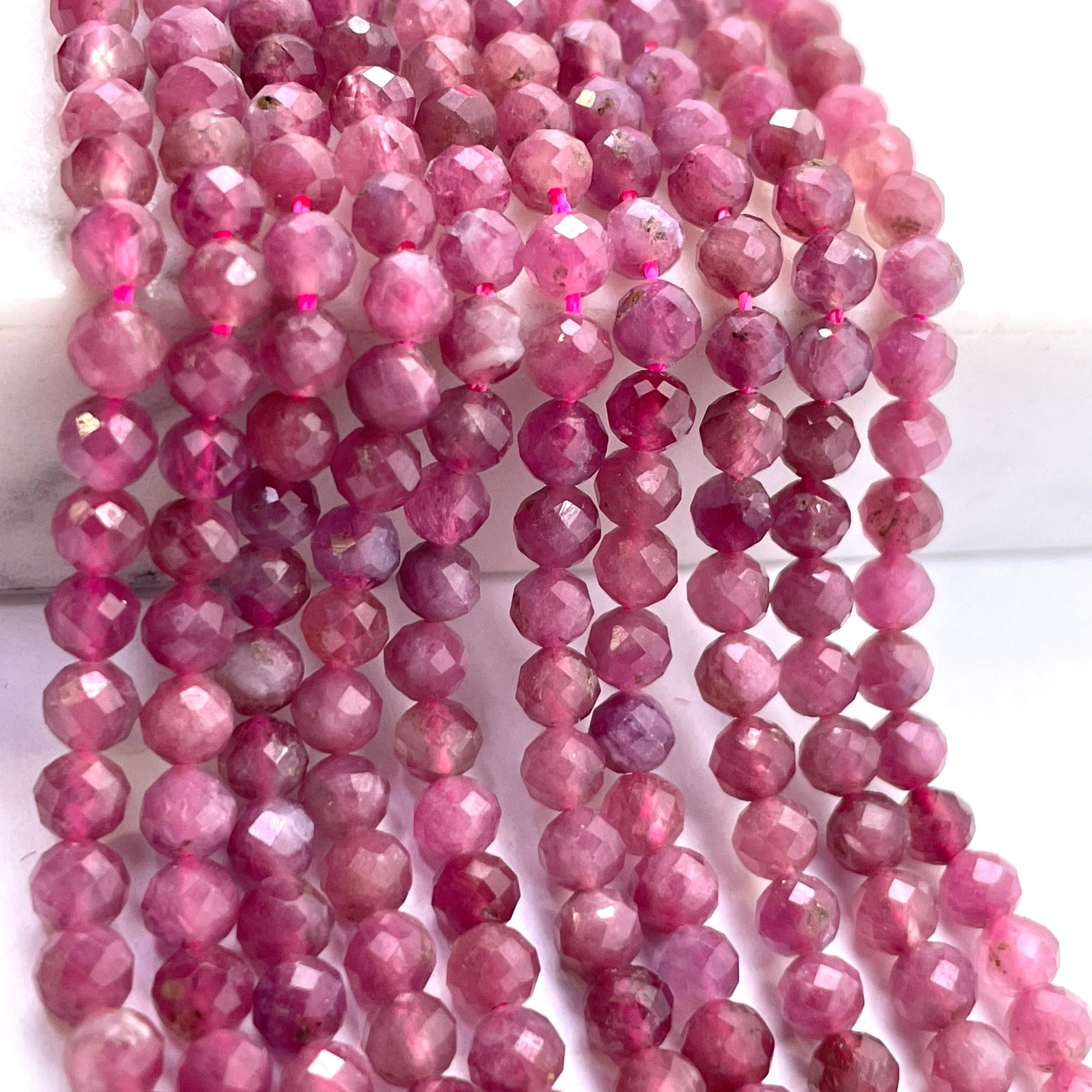 Faceted pink tourmaline gemstone beads strung in multiple strands, displayed on a white surface.