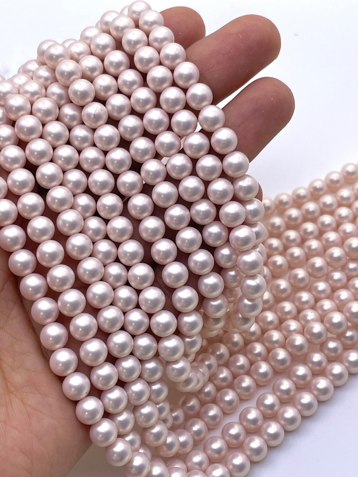 A hand holding a dense bundle of light pink shell pearl beads, with more strands draped across a white surface.
