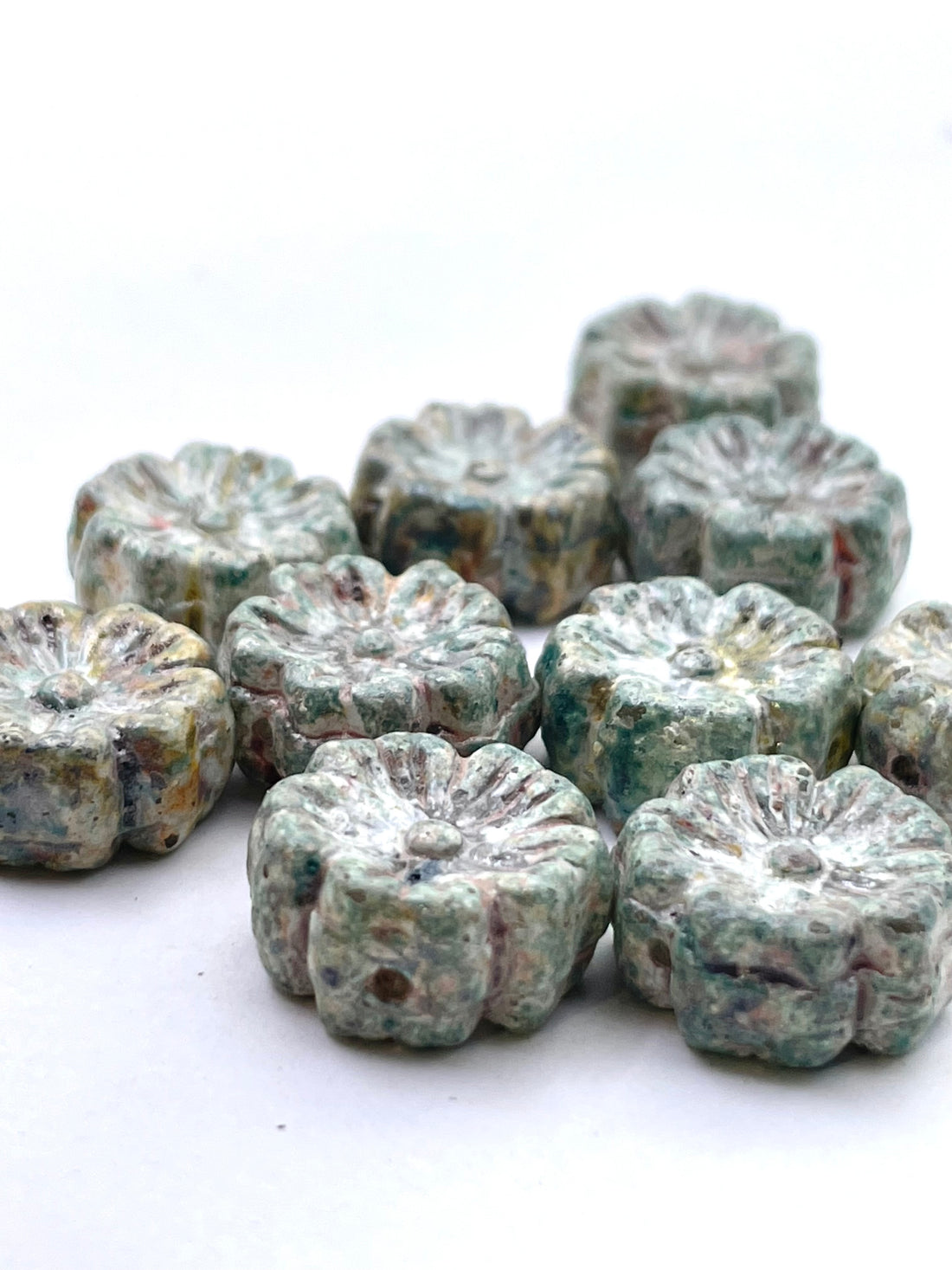 A group of small, textured, flower-shaped beads in a mottled green and gray stone-like finish, arranged on a plain white background.