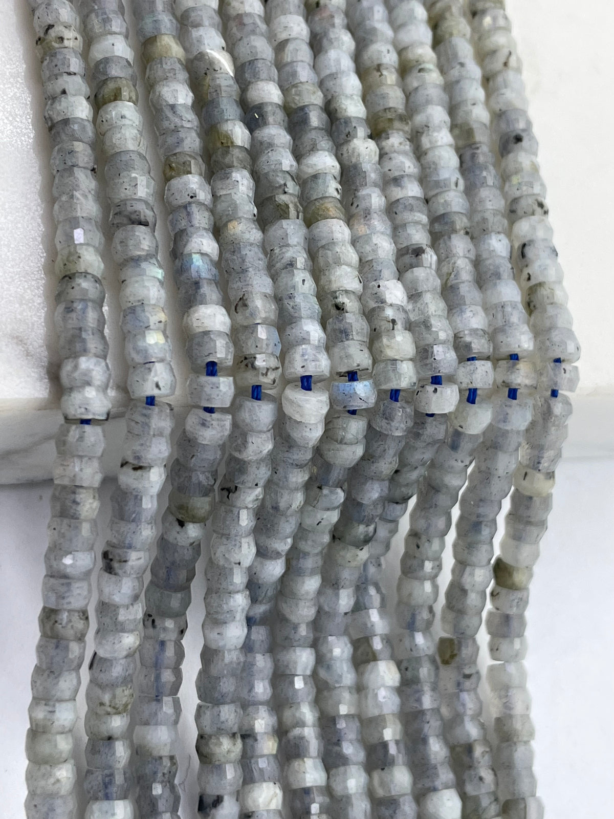 Multiple strands of faceted labradorite beads in natural gray, white, and blue-gray tones, laid out vertically on a white background.