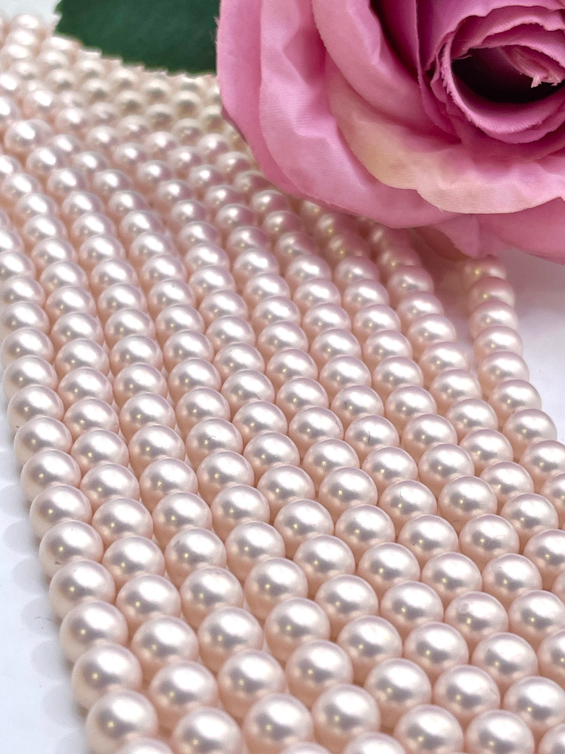 A hand holding a dense bundle of light pink shell pearl beads, with more strands draped across a white surface.