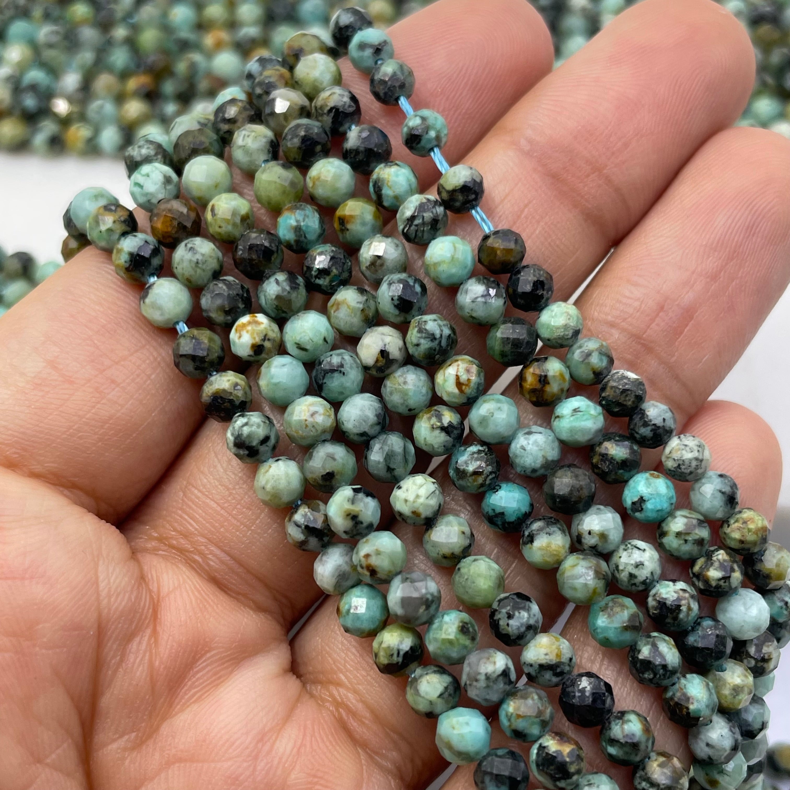 Faceted round african turquoise beads in green, and black marbled pattern, strung on a light blue cord and held in a hand.