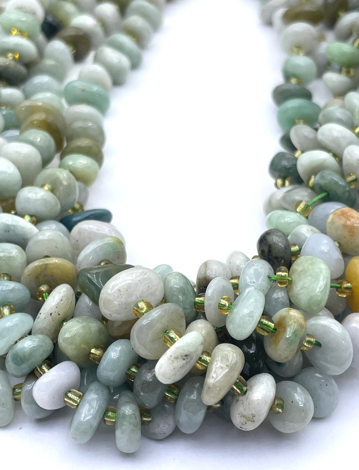 A close-up of a multi-strands of burma jade made of polished, irregular-shaped gemstone chips in shades of sage green, gray, white, and light blue, separated by small gold spacer beads, on a plain white background.