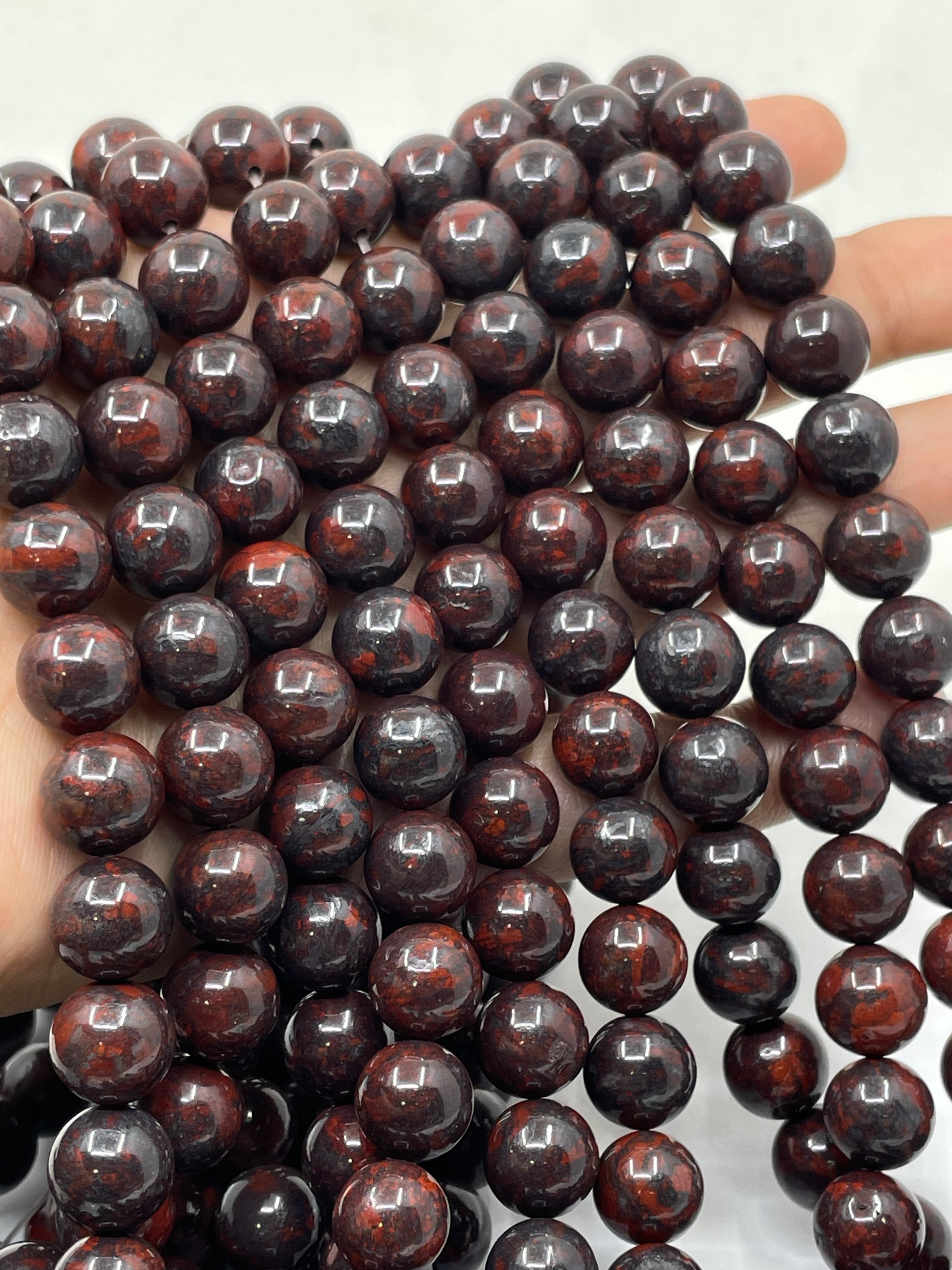 A close-up of glossy dark reddish-brown round brecciated jasper beads held in a hand against a light background.
