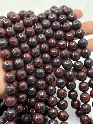 A close-up of glossy dark reddish-brown round brecciated jasper beads held in a hand against a light background.