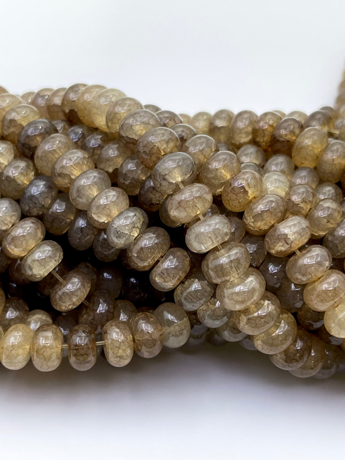 Smooth round glass beads in a smoky brown and translucent amber tone, arranged in overlapping strands on a plain white background.