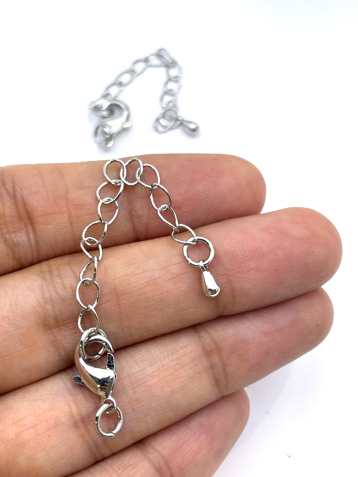 A silver chain bracelet with a lobster clasp and extension chain, held in a person's hand against a white background.