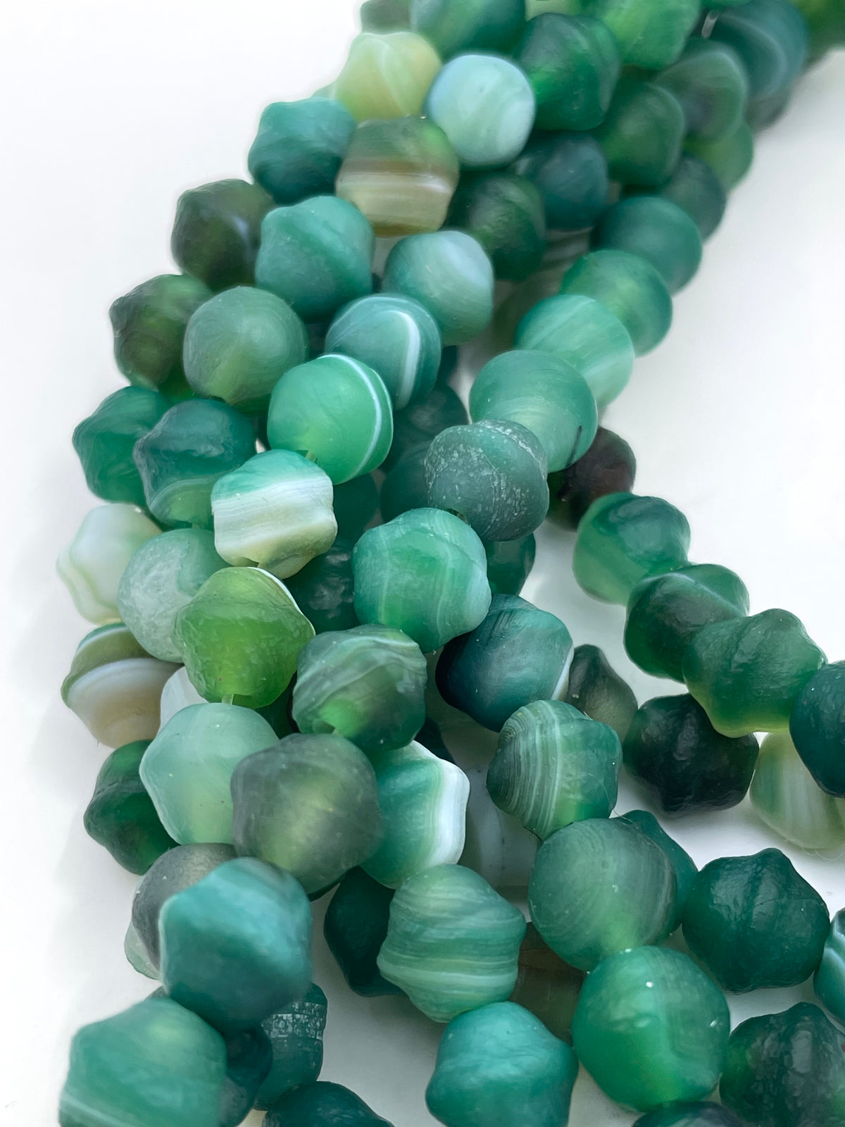 Green agate stone beads with natural banding and marbled textures, arranged in a diagonal line on a white background.