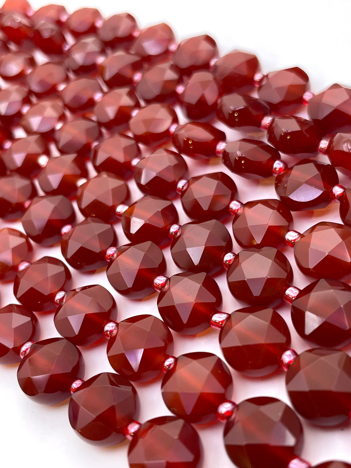 Faceted carnelian gemstone beads arranged in overlapping rows on a white background.