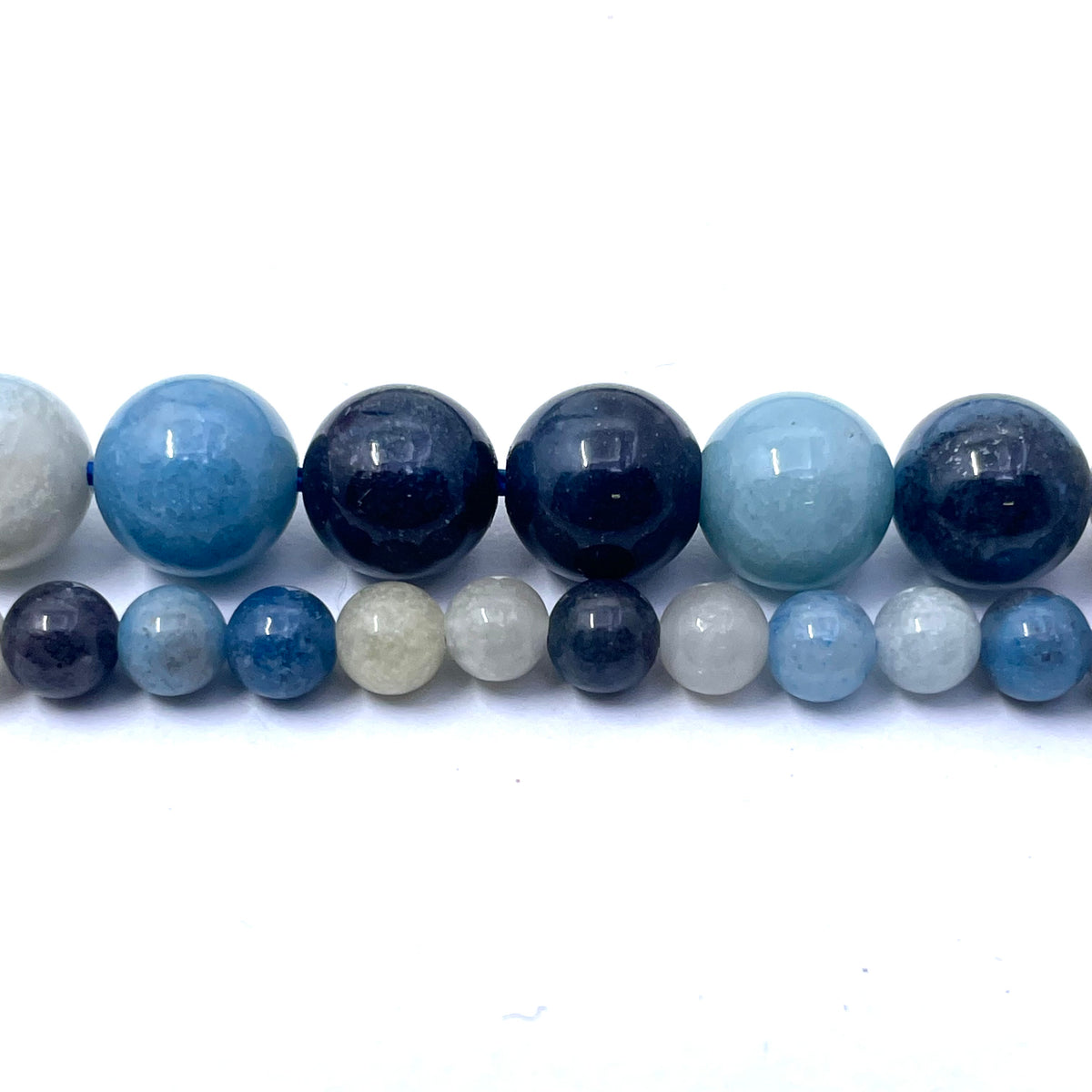 A strand of polished round gemstone beads in various sizes, featuring shades of light blue, dark navy, and white, arranged in two rows on a plain white background.
