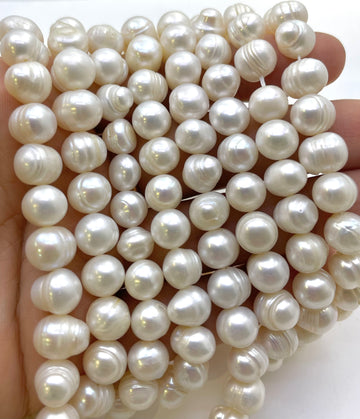 A close-up of a hand holding a dense bundle of glossy, irregular-shaped white freshwater pearls.