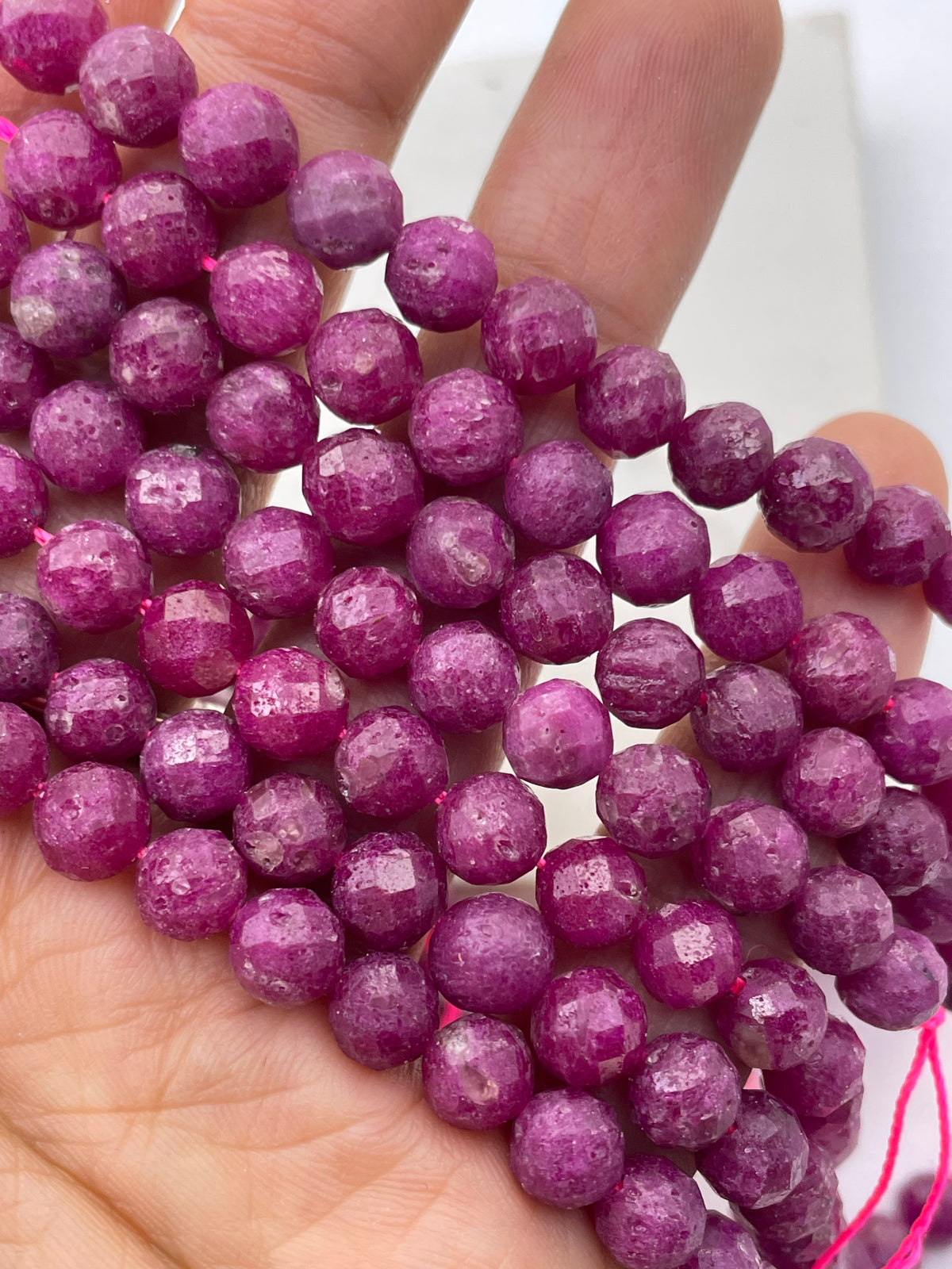 Faceted round ruby gemstone beads in a vibrant magenta-pink color, draped over and held in a person's hand