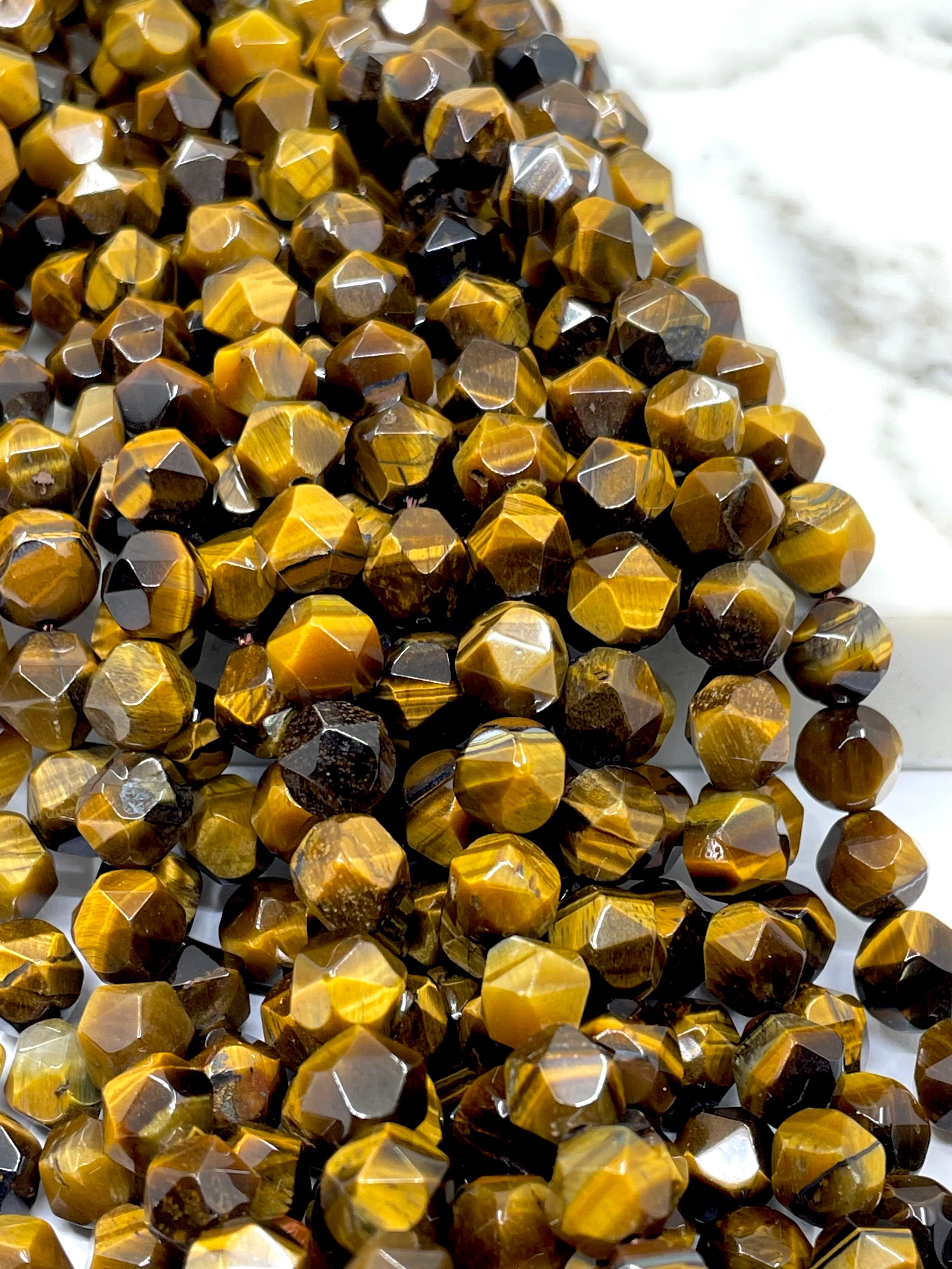 Faceted tiger's eye gemstone beads in a gold and brown color combination, arranged on a white marble surface.