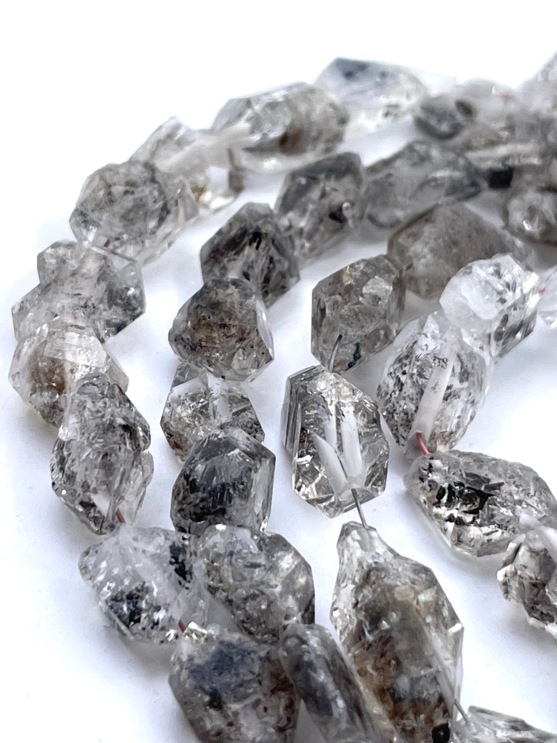 Rough clear herkimer diamond beads with visible inclusions and smoky gray tones, arranged on a white background.
