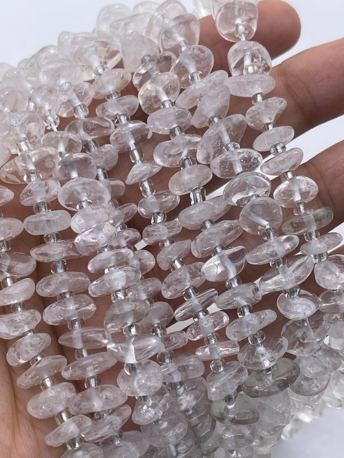 A close-up of a hand holding a strand of clear, disc-shaped quartz gemstone beads separated by small silver spacer rings.
