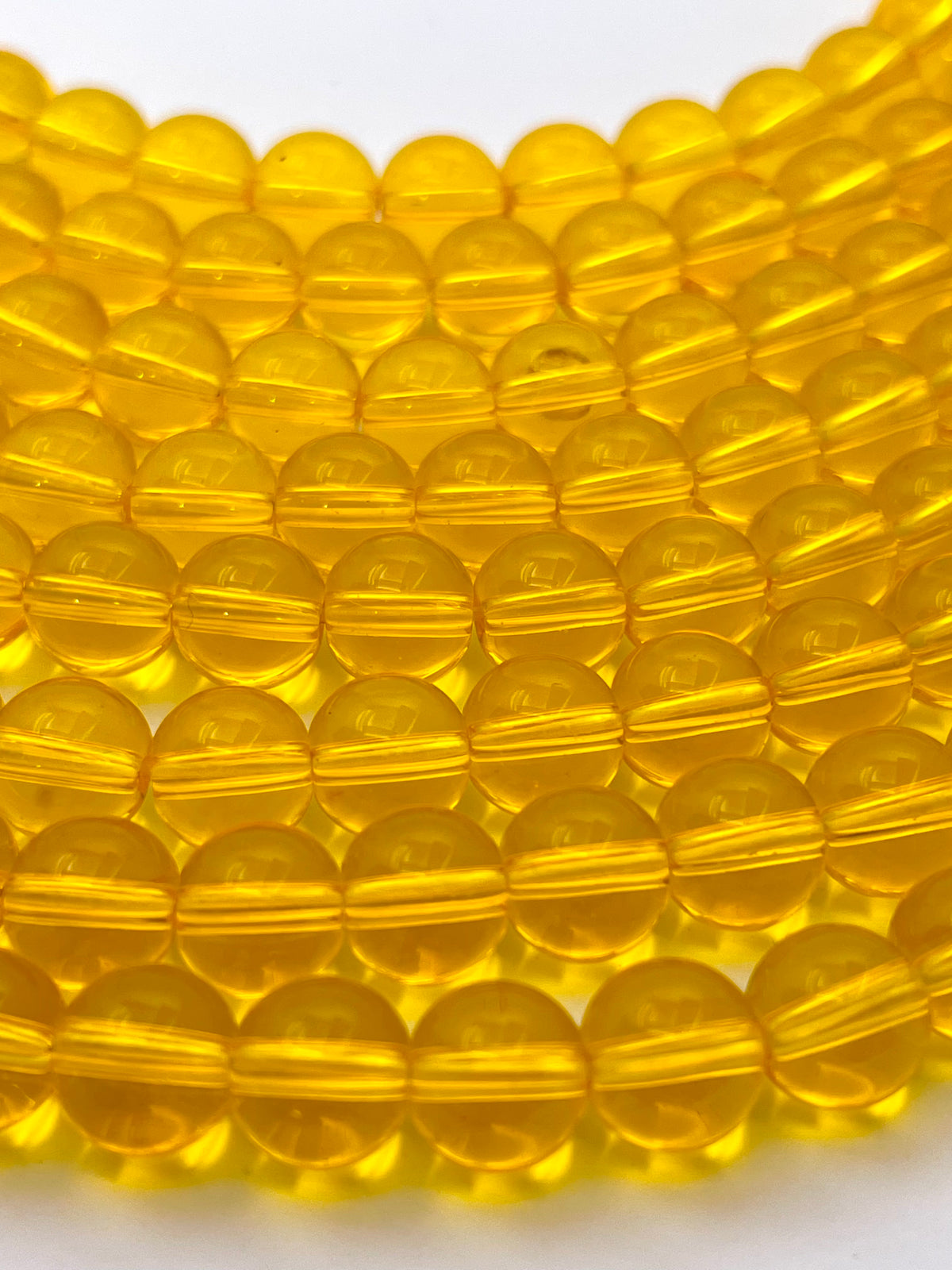 A close-up of translucent yellow glass beads arranged in rows on a white background.
