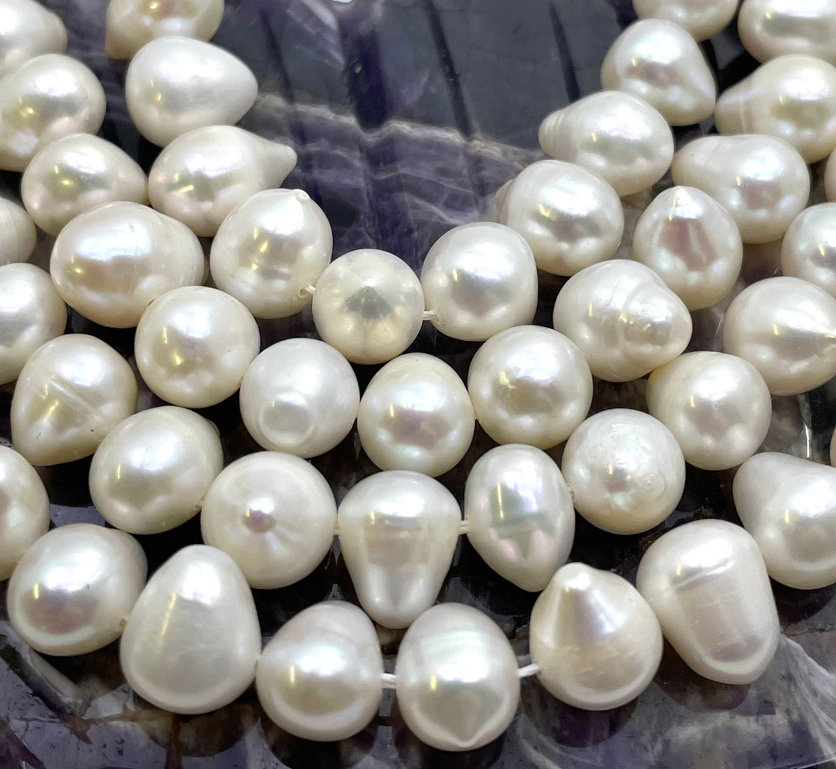 A close-up of irregular white baroque pearls strung on a cord, arranged on a dark marbled surface.