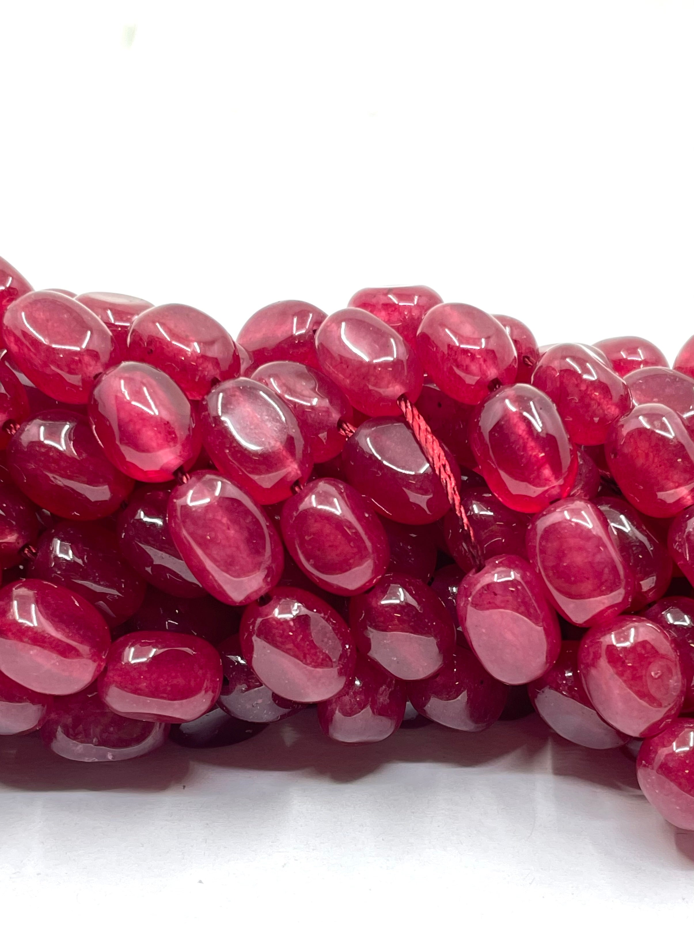 A close-up of glossy, translucent deep pinkish-red oval beads strung on a cord, set against a plain white background.