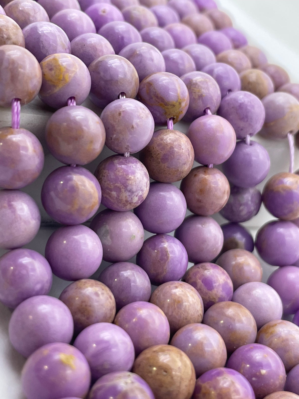 Close-up of a strand of polished round phosphosiderite beads in lavender purple and light brown with natural marbled patterns, strung on a cord.