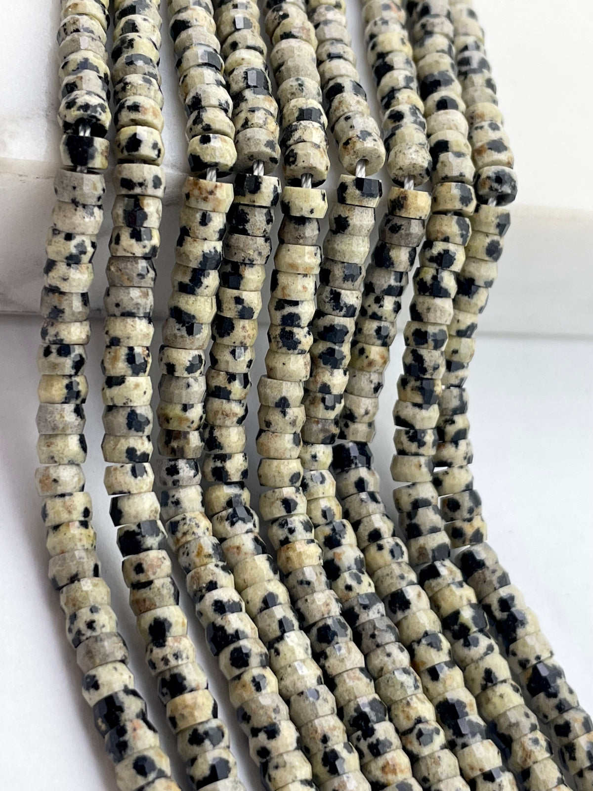 Multiple strands of small cylindrical beads made from dalmation jasper arranged vertically on a white surface.