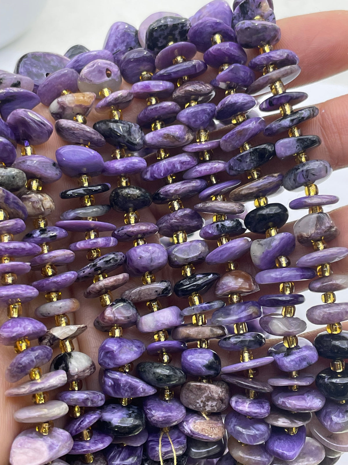 Charoite chip bead strands with gold spacer beads held in a hand.