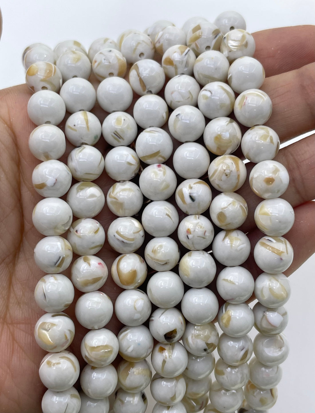 Ivory round mop beads with natural tan and brown inclusions, arranged in diagonal rows on a white background.