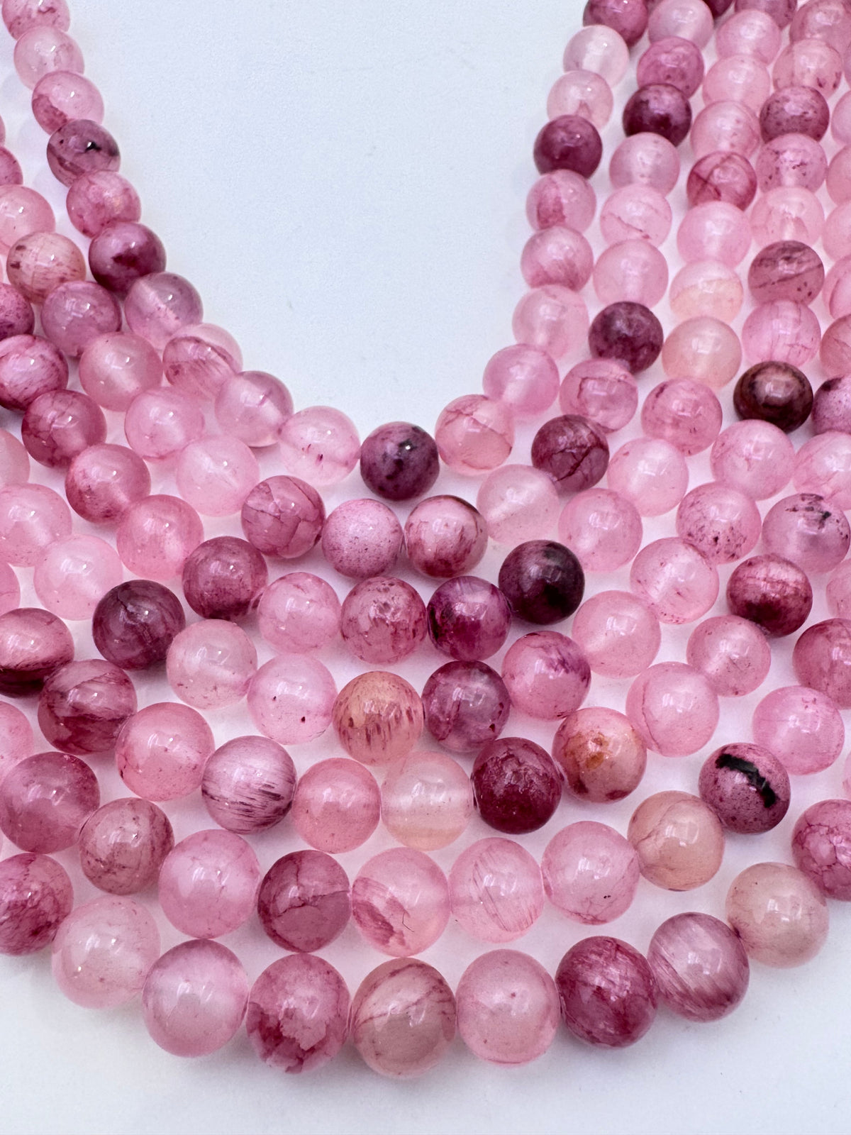 Multiple strands of round pink persian jade gemstone beads with natural marbling and inclusions, arranged on a plain white background.